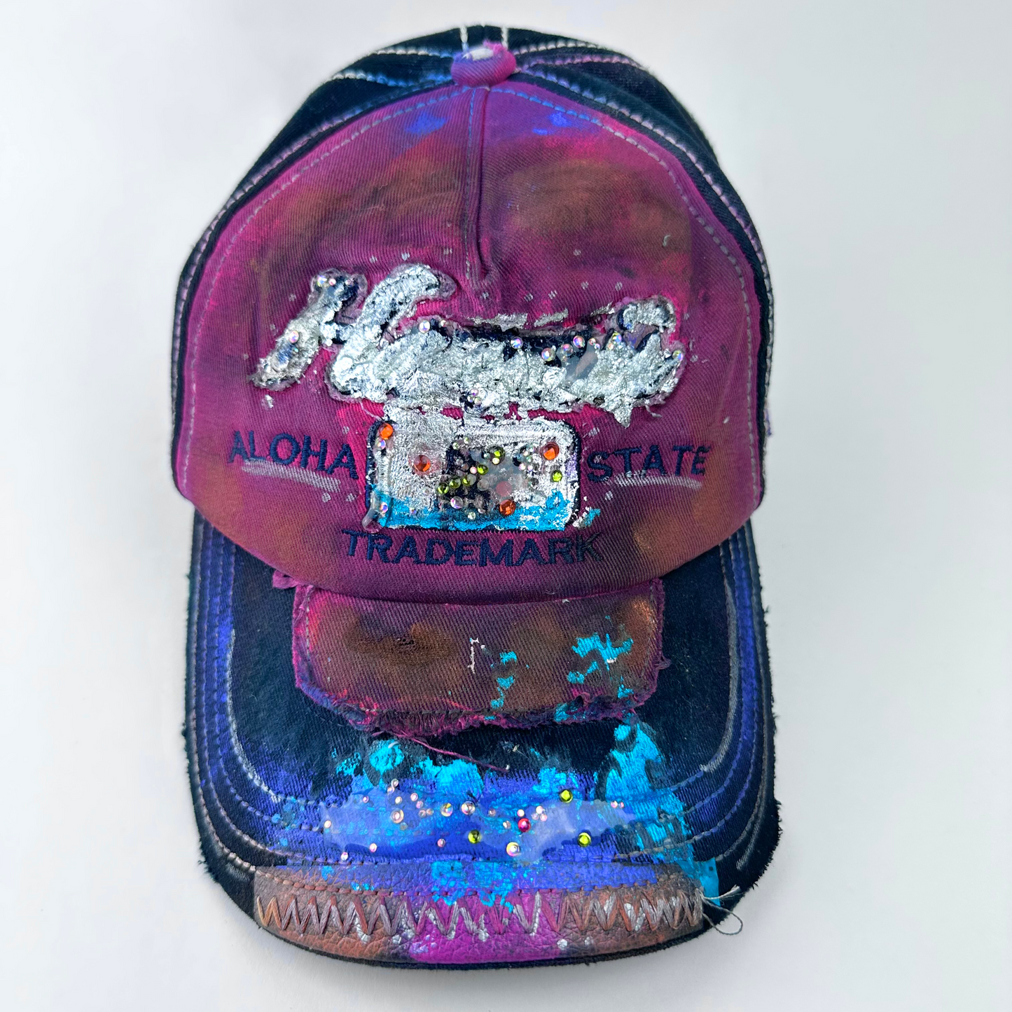 ASTROBOI* 'Hibiscus' red and black Y2K Hawaii rhinestone hat with silver embroidered 'Hawaii ALOHA STATE TRADEMARK' text, purple and pink paint splatter, and metallic rhinestone embellishments, front view.