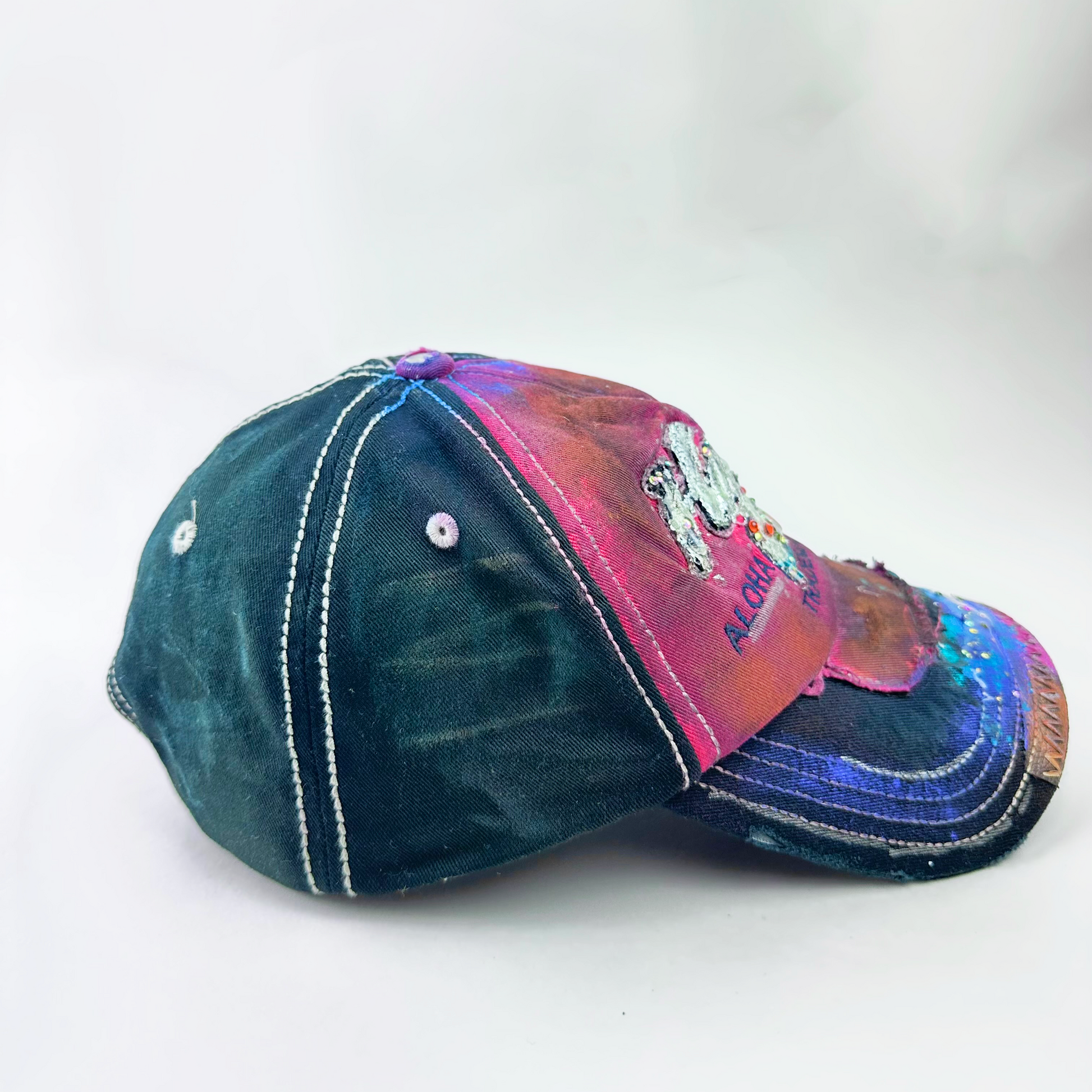 ASTROBOI* 'Hibiscus' red and black Y2K Hawaii rhinestone hat with silver embroidered 'Hawaii ALOHA STATE TRADEMARK' text, purple and pink paint splatter, and metallic rhinestone embellishments, left side.