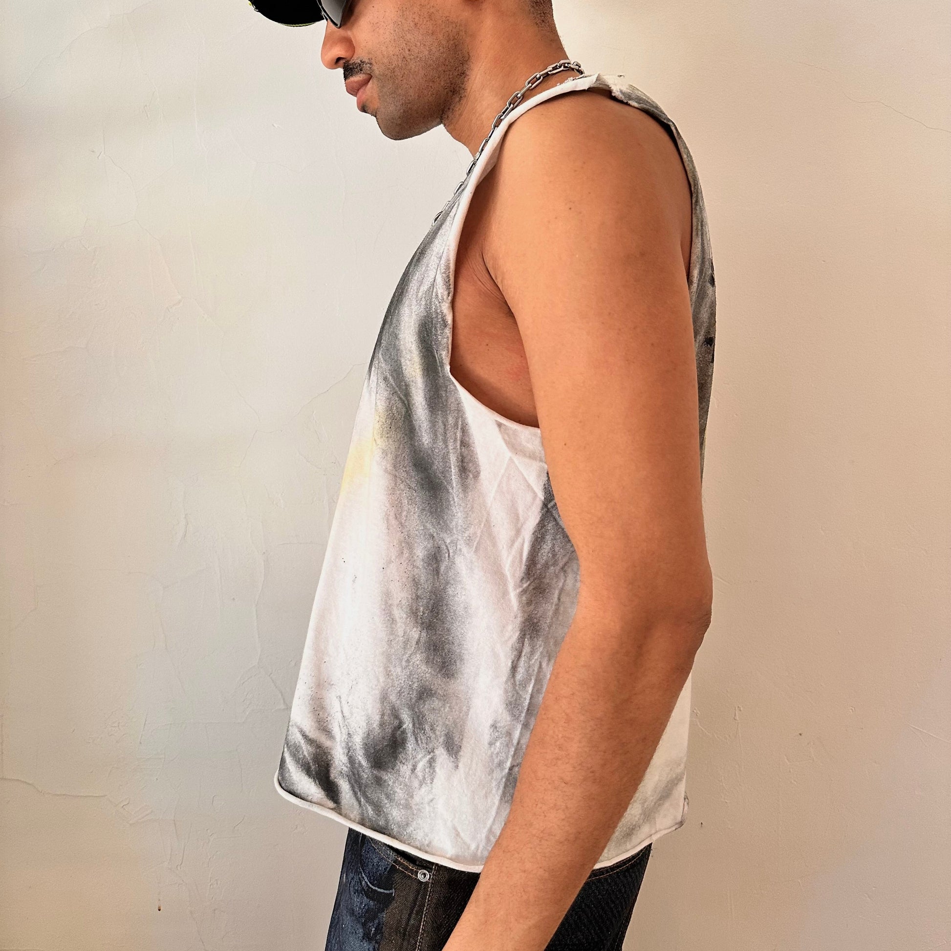 Left side detail of ASTROBOI* x Fox Racing tank showing airbrush streak treatment, punched holes, and raw hem on white motocross fabric.