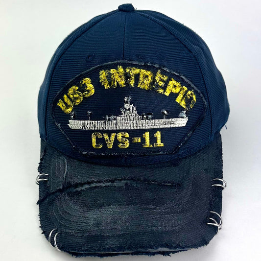 Front of ASTROBOI* upcycled Navy blue and black USS Intrepid CVS-11 snapback hat with silver rhinestone-embellished front patch, stainless steel brim piercings, and hand-painted black visor on a neutral background.