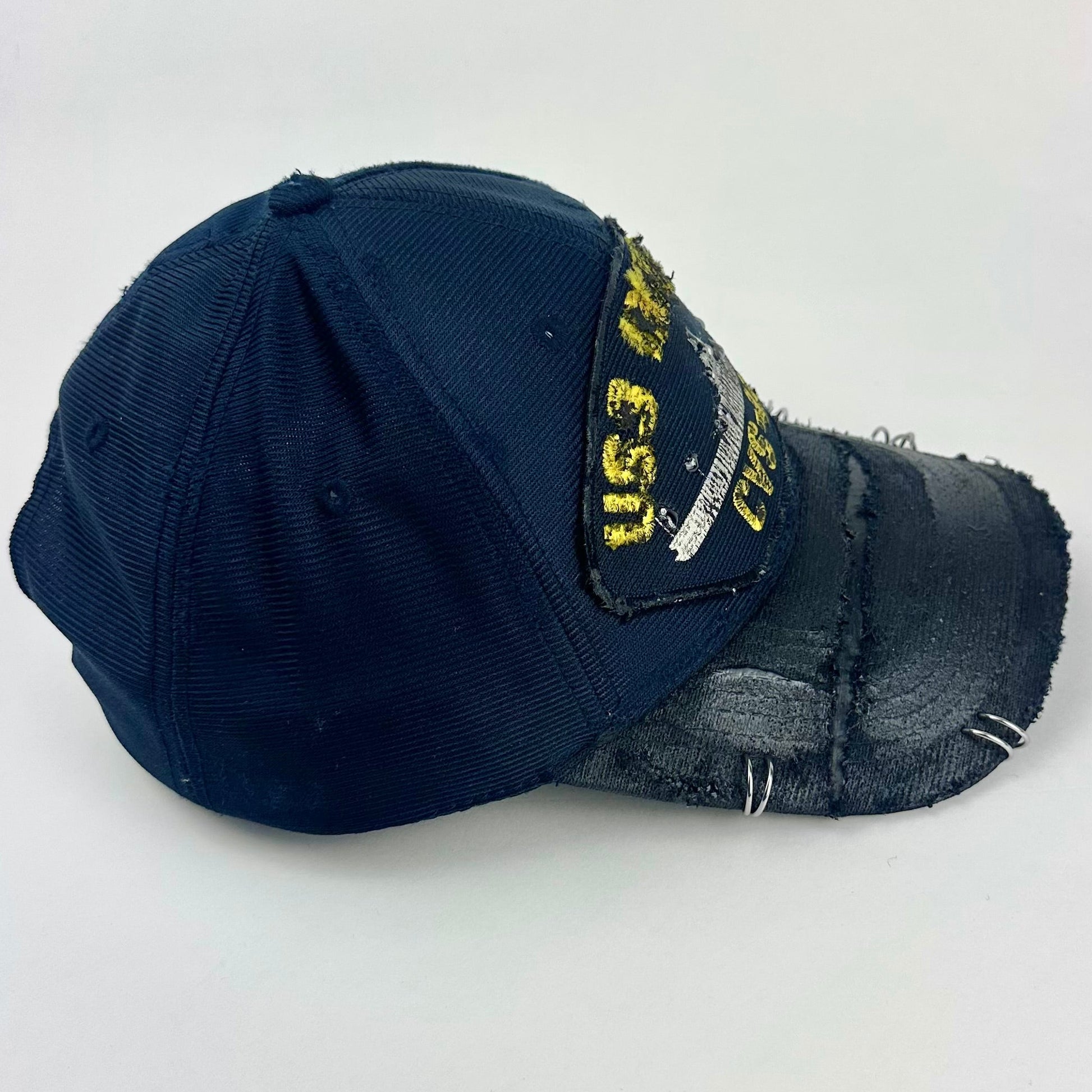 Right side of ASTROBOI* upcycled Navy blue and black USS Intrepid CVS-11 snapback hat with silver rhinestone-embellished front patch, stainless steel brim piercings, and hand-painted black visor on a neutral background.