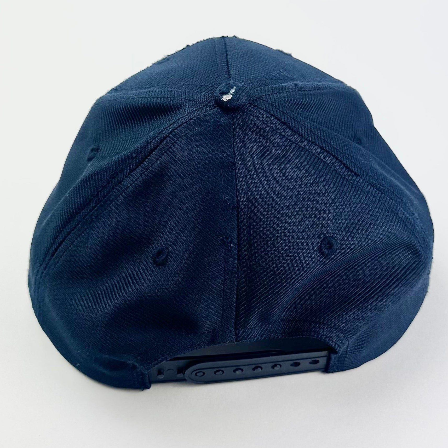 Top of ASTROBOI* upcycled Navy blue and black USS Intrepid CVS-11 snapback hat with silver rhinestone-embellished front patch, stainless steel brim piercings, and hand-painted black visor on a neutral background.