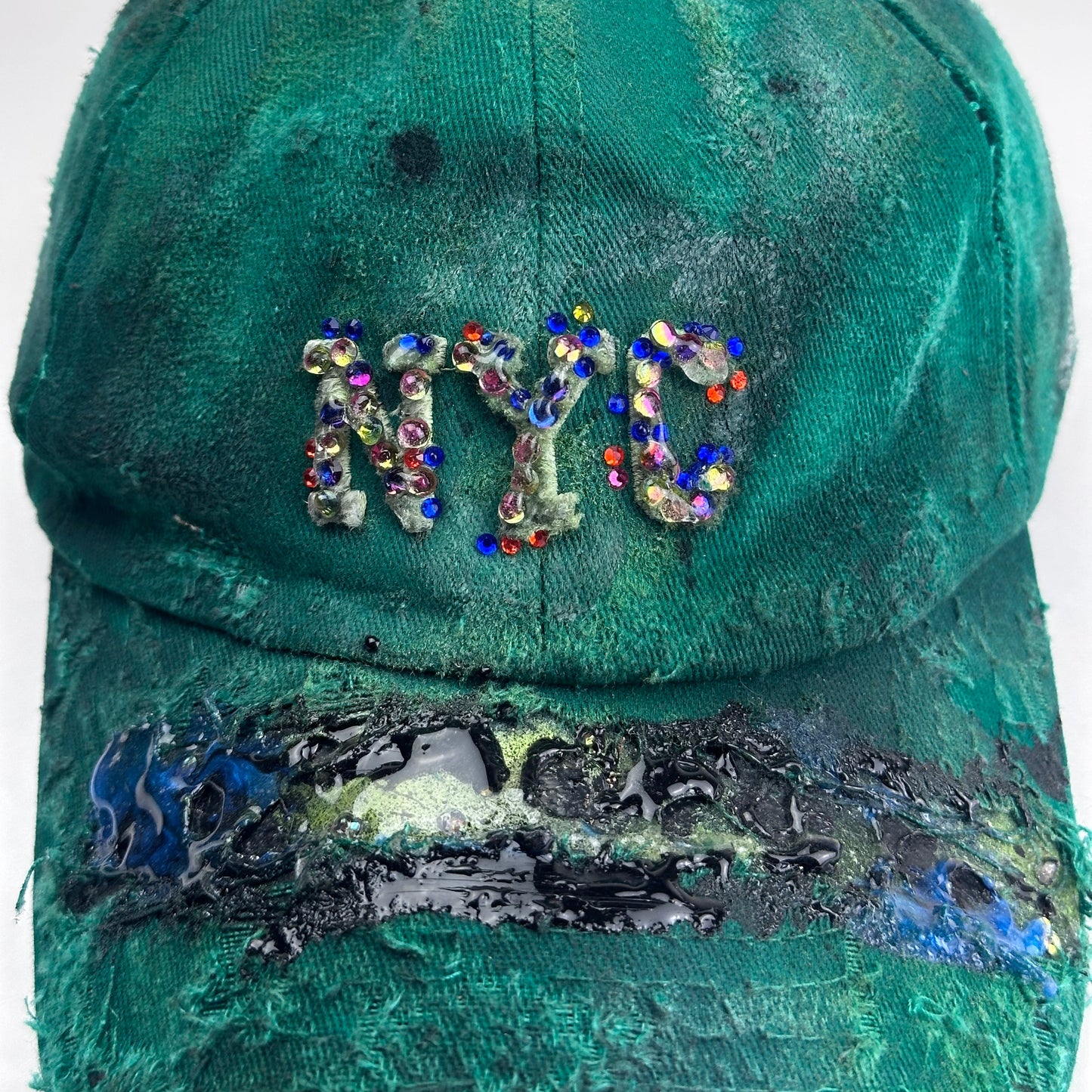Logo detail of ASTROBOI* Smith NYC green distressed hat with clear rhinestone logo, custom paint treatment and blue black resin textured visor.