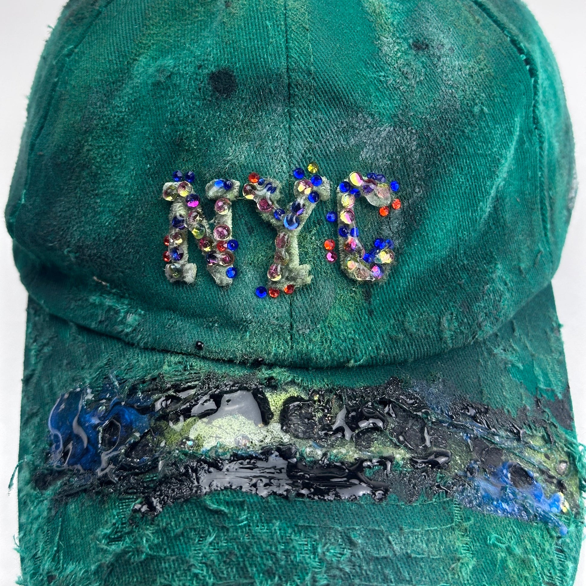 Logo detail of ASTROBOI* Smith NYC green distressed hat with clear rhinestone logo, custom paint treatment and blue black resin textured visor.