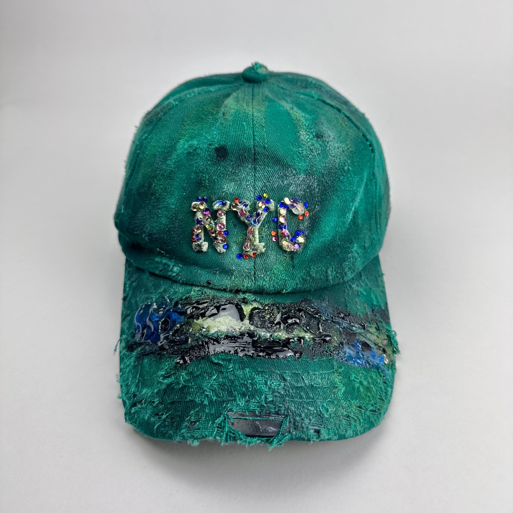 Frontal image of ASTROBOI* Smith NYC green distressed hat with clear rhinestone logo, custom paint treatment and blue black resin textured visor.