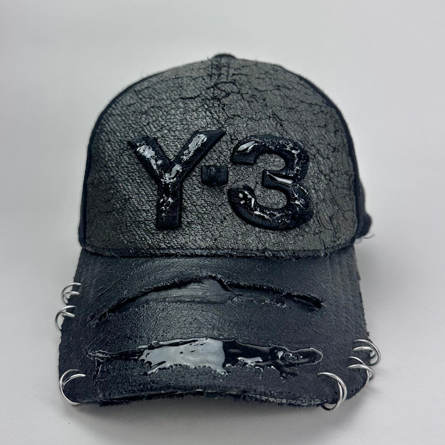 Front of ASTROBOI* x Y-3 black distressed baseball cap with stainless steel piercings, cracked chrome effect, painted flannel, and center Y-3 logo.