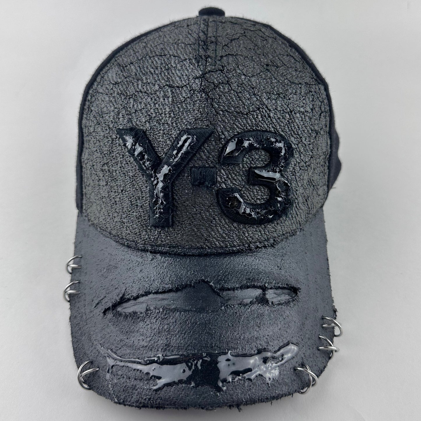 Front of ASTROBOI* x Y-3 black distressed baseball cap with stainless steel piercings, cracked chrome effect, painted flannel, and center Y-3 logo.