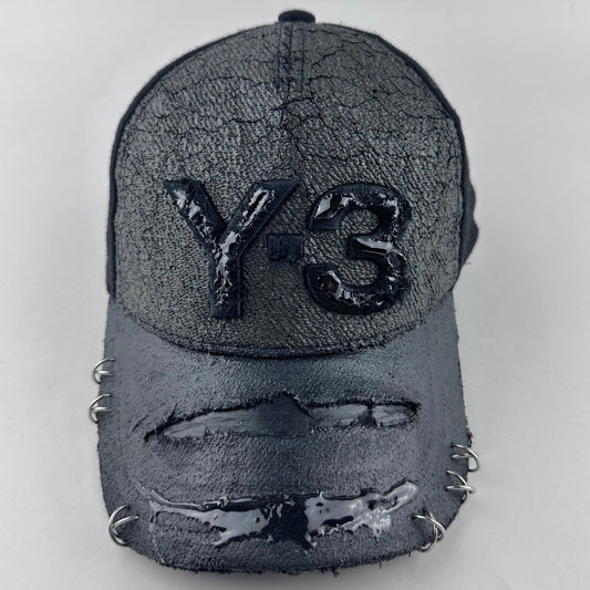 Front of ASTROBOI* x Y-3 black distressed baseball cap with stainless steel piercings, cracked chrome effect, painted flannel, and center Y-3 logo.