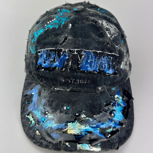 Cover front image of ASTROBOI* Plavala black iridescent hat with rhinestone NYC logos, metallic paint and black clear resin creating a hazy milky way effect.