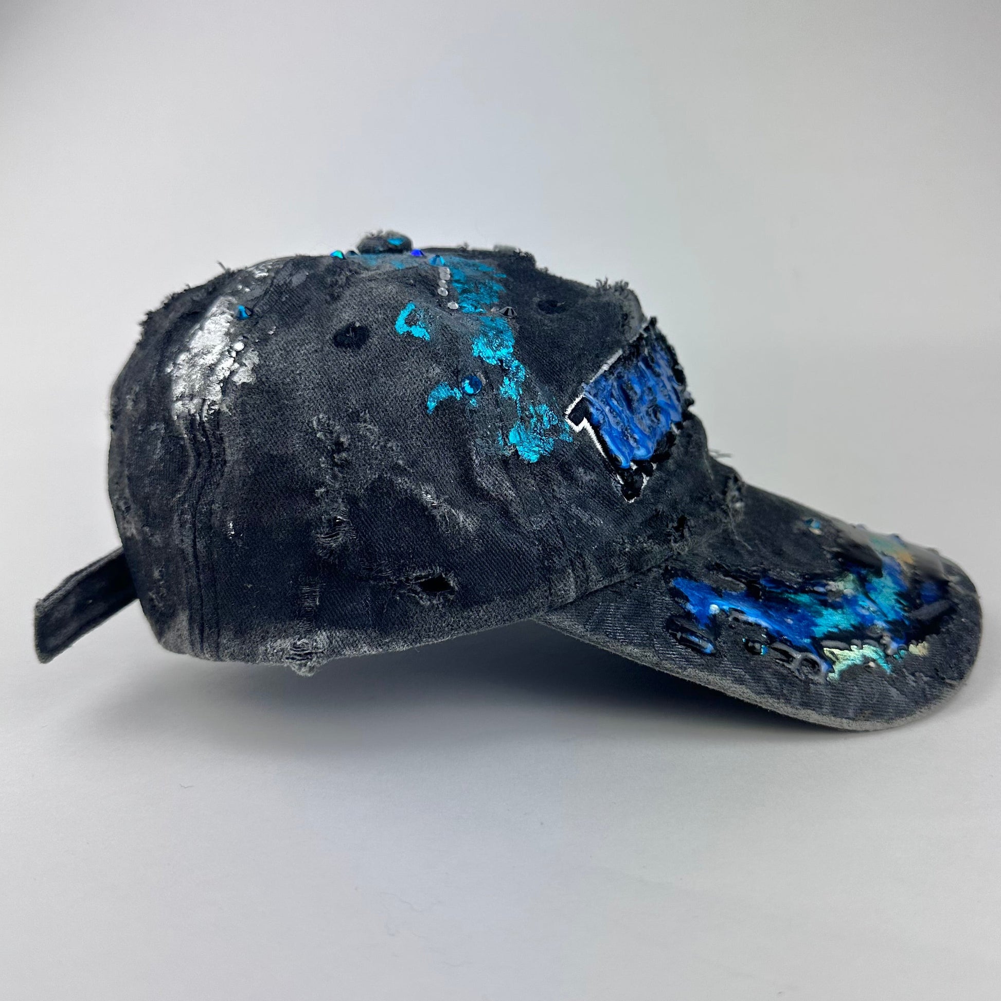 Right side of ASTROBOI* Plavala black iridescent hat with rhinestone NYC logos, metallic paint and black clear resin creating a hazy milky way effect.