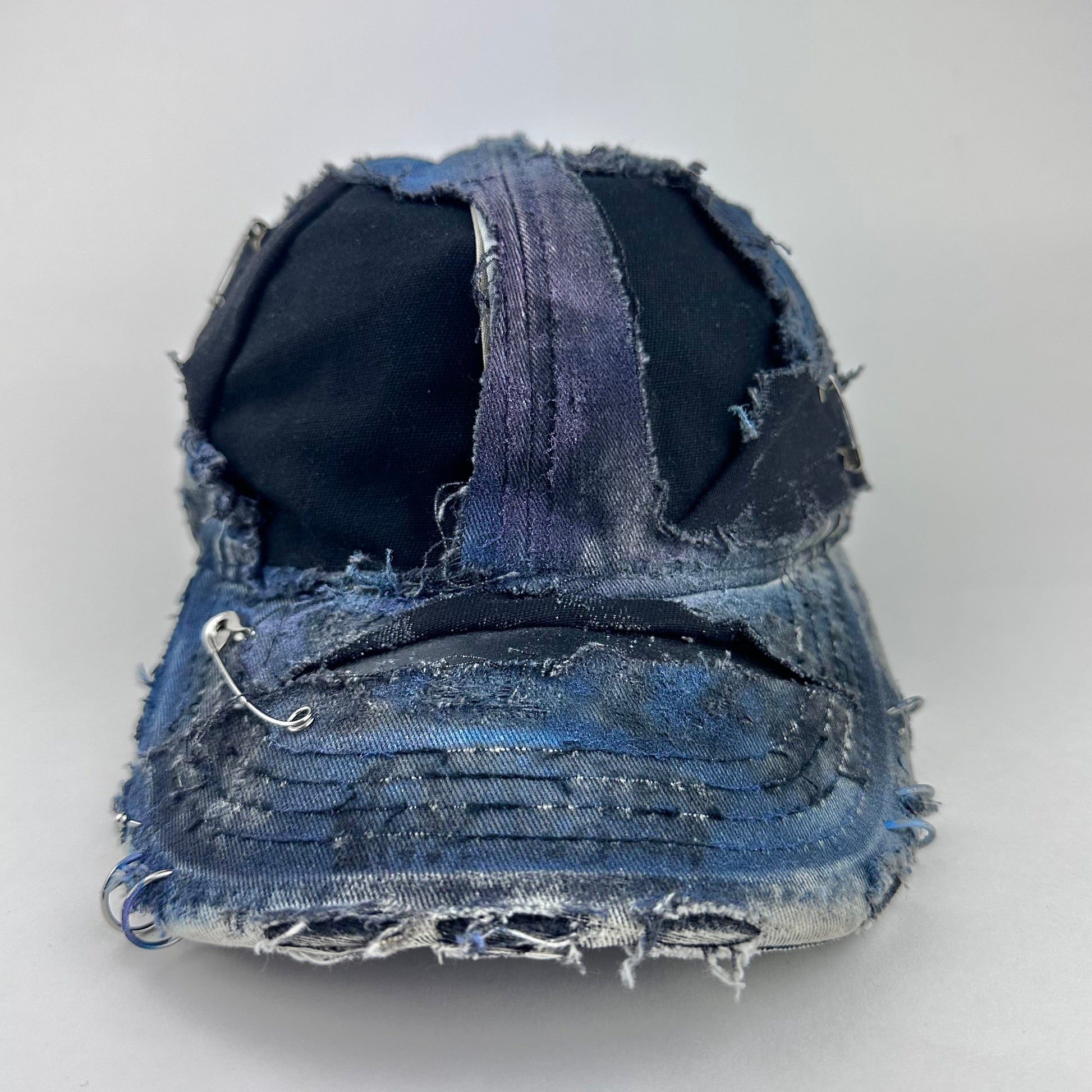 Front image of ASTROBOI* Nebulous Cloud black hat with rainbow airbrush denim, safety pins and silver steel piercings on distressed grunge design.