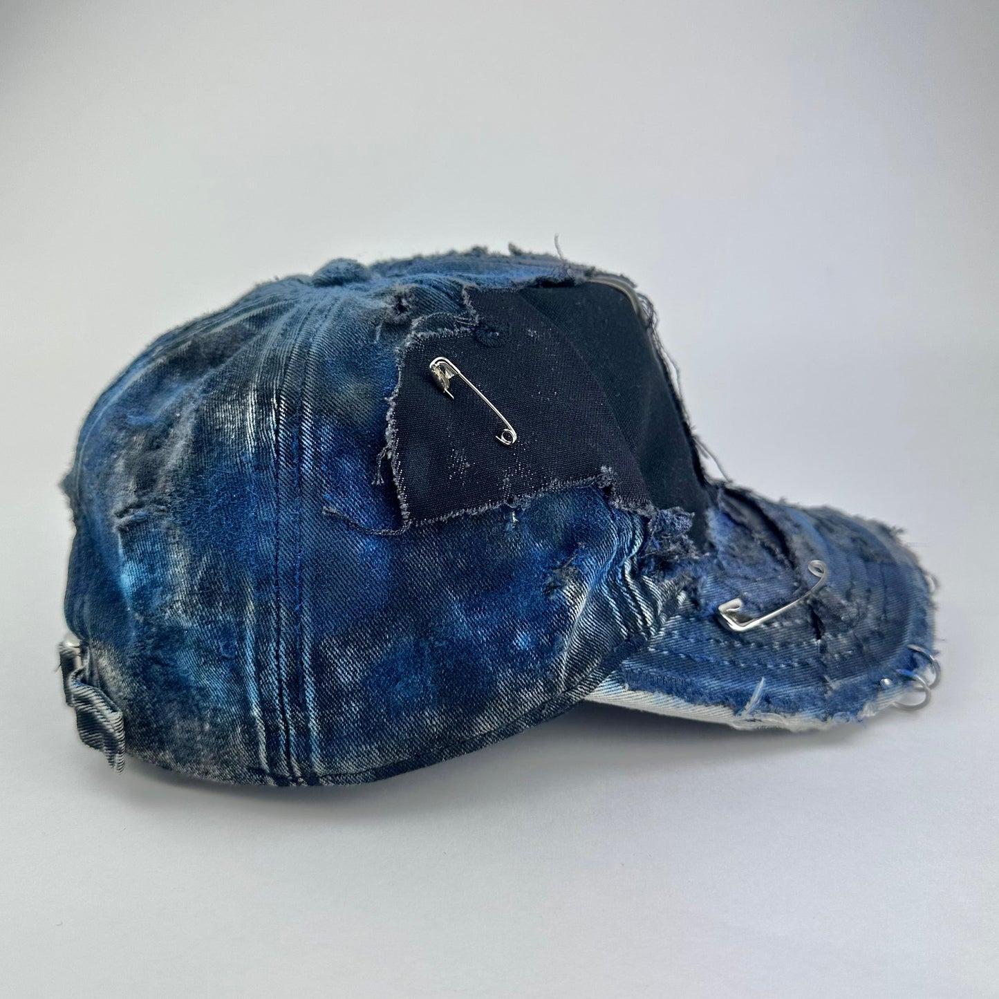 Right side of ASTROBOI* Nebulous Cloud black hat with rainbow airbrush denim, safety pins and silver steel piercings on distressed grunge design.