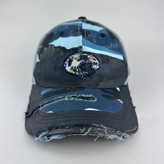 Cover image of ASTROBOI* Costa blue and white camo rhinestone trucker hat with black waxed tattoo print, mesh back panels, adjustable strap, custom NYC piece