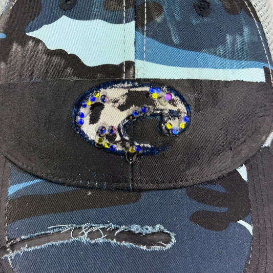 Logo detail on ASTROBOI* Costa blue and white camo rhinestone trucker hat with black waxed tattoo print, mesh back panels, adjustable strap, custom NYC piece