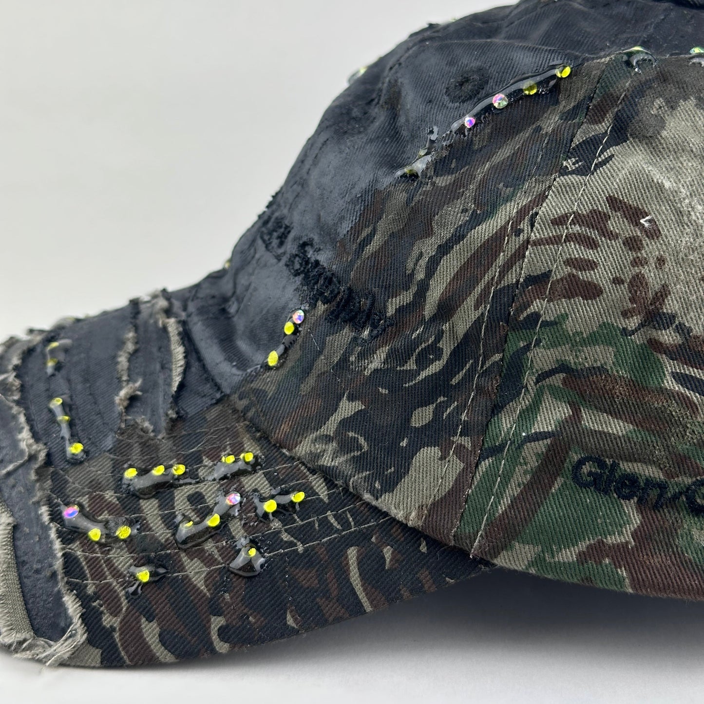 Flay lay front rhinestone detail of ASTROBOI* L&L Supply green RealTree camo utility hat with purple and green rhinestones sealed in resin and black tattoo print detailing