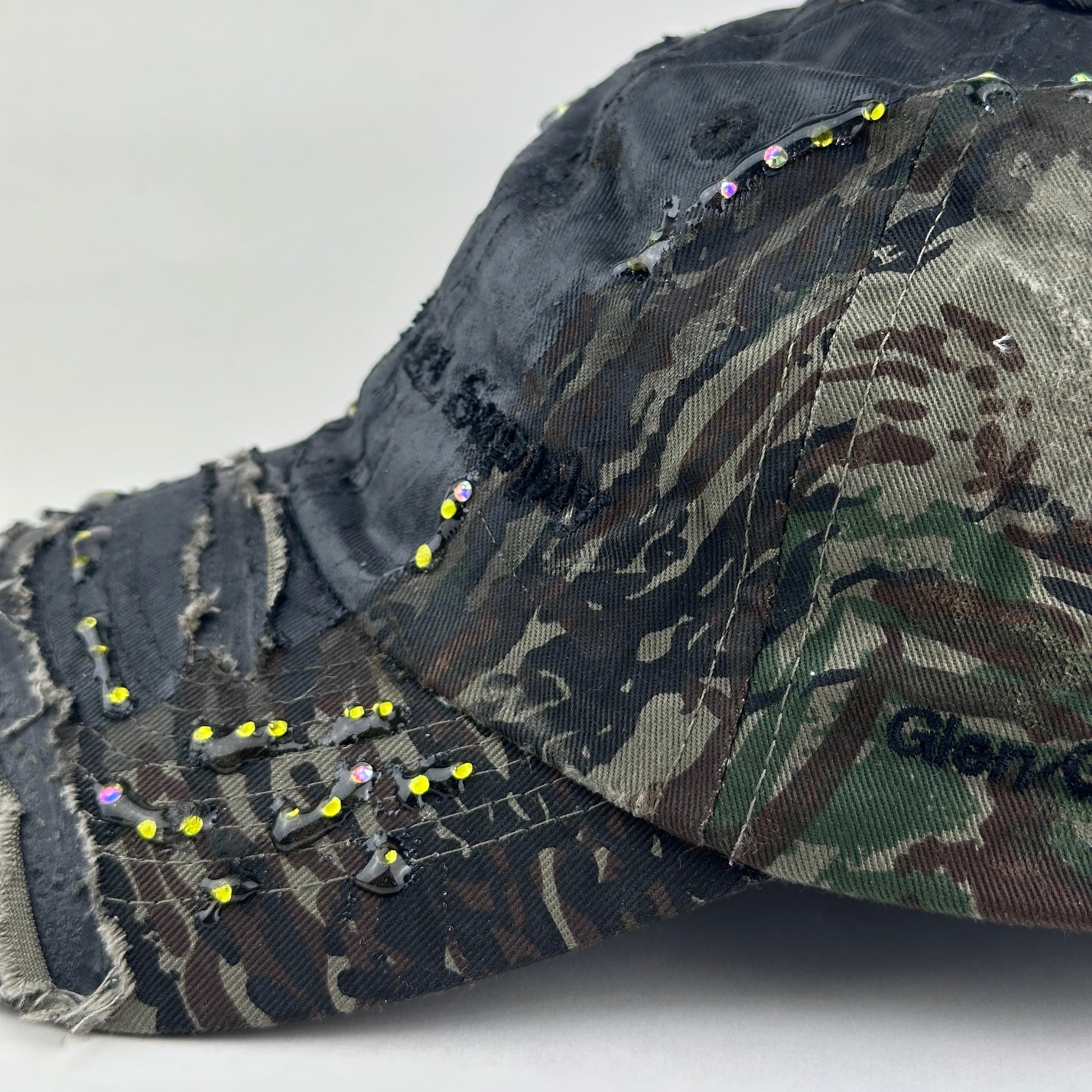 Flay lay front rhinestone detail of ASTROBOI* L&L Supply green RealTree camo utility hat with purple and green rhinestones sealed in resin and black tattoo print detailing