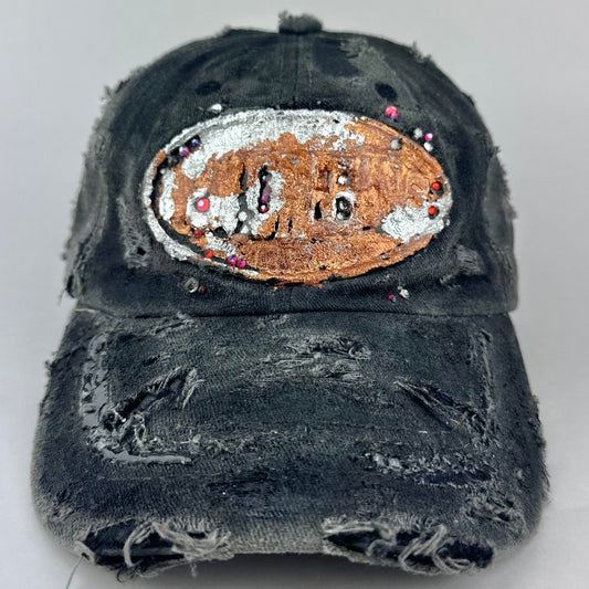 Front of ASTROBOI* NOCU black distressed hat with copper metallic New Orleans logo, red and purple rhinestones and glossy resin coated visor.