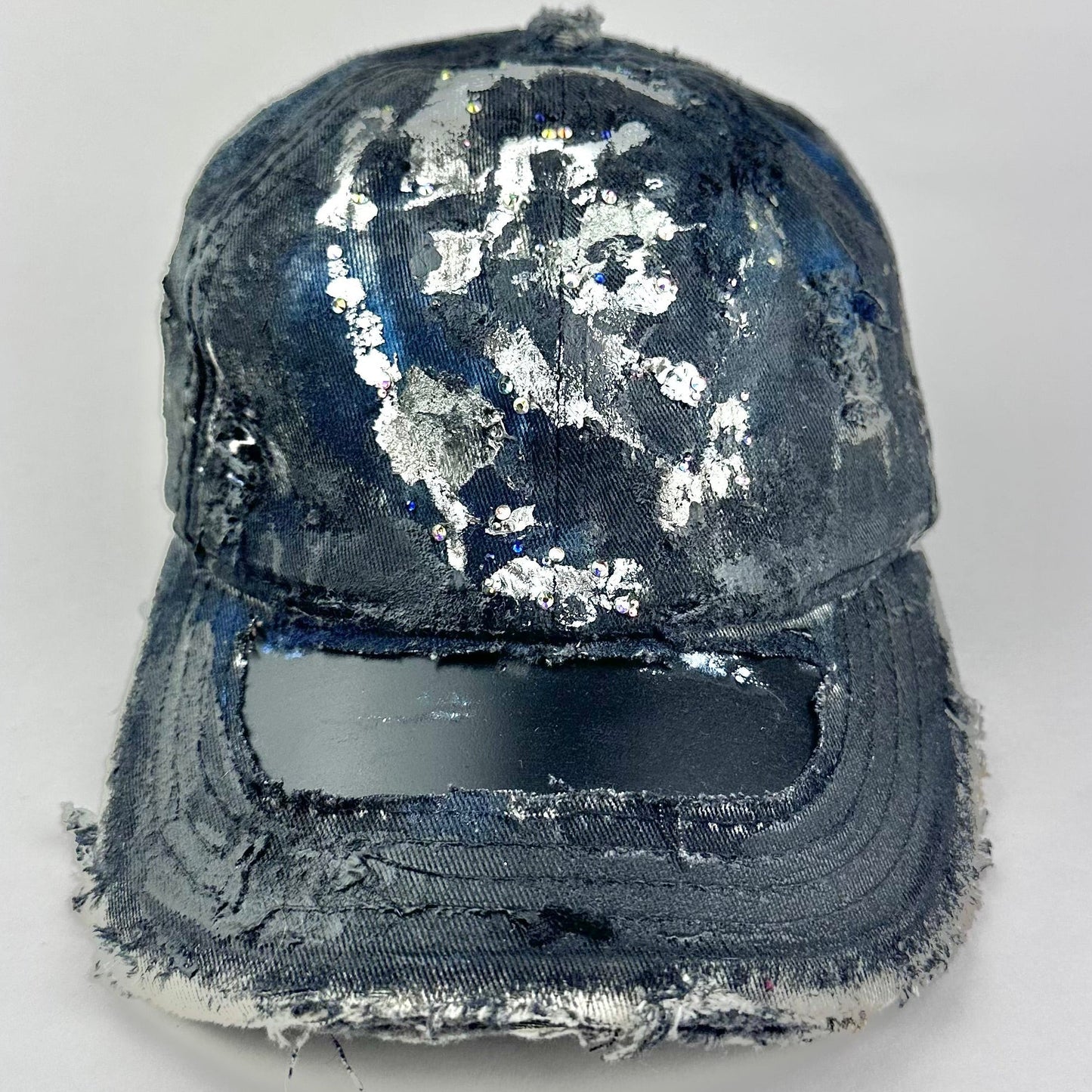 Front flay lay on Black acid-washed denim hat with silver paint accents, multicolored rhinestones, and a ripped visor seam, customized by ASTROBOI* STUDIO.