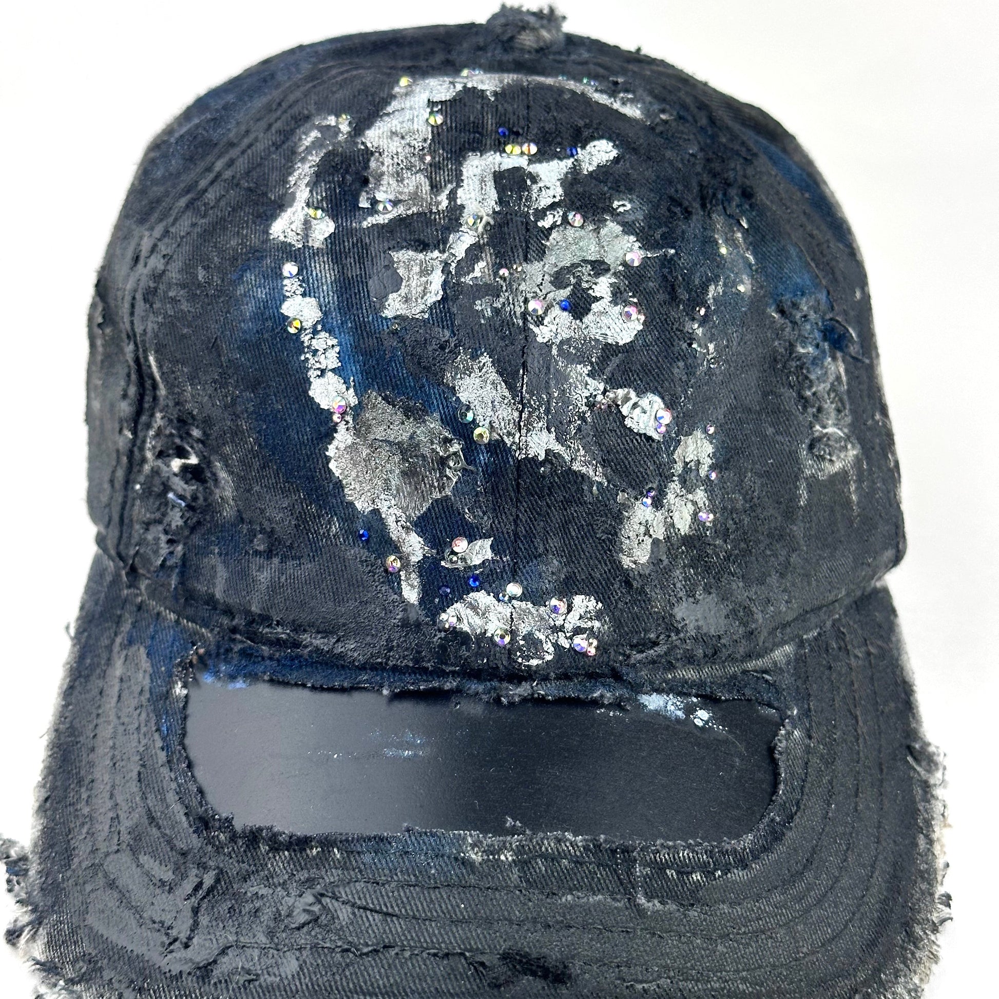 Flay lay front detail on Black acid-washed denim hat with silver paint accents, multicolored rhinestones, and a ripped visor seam, customized by ASTROBOI* STUDIO.