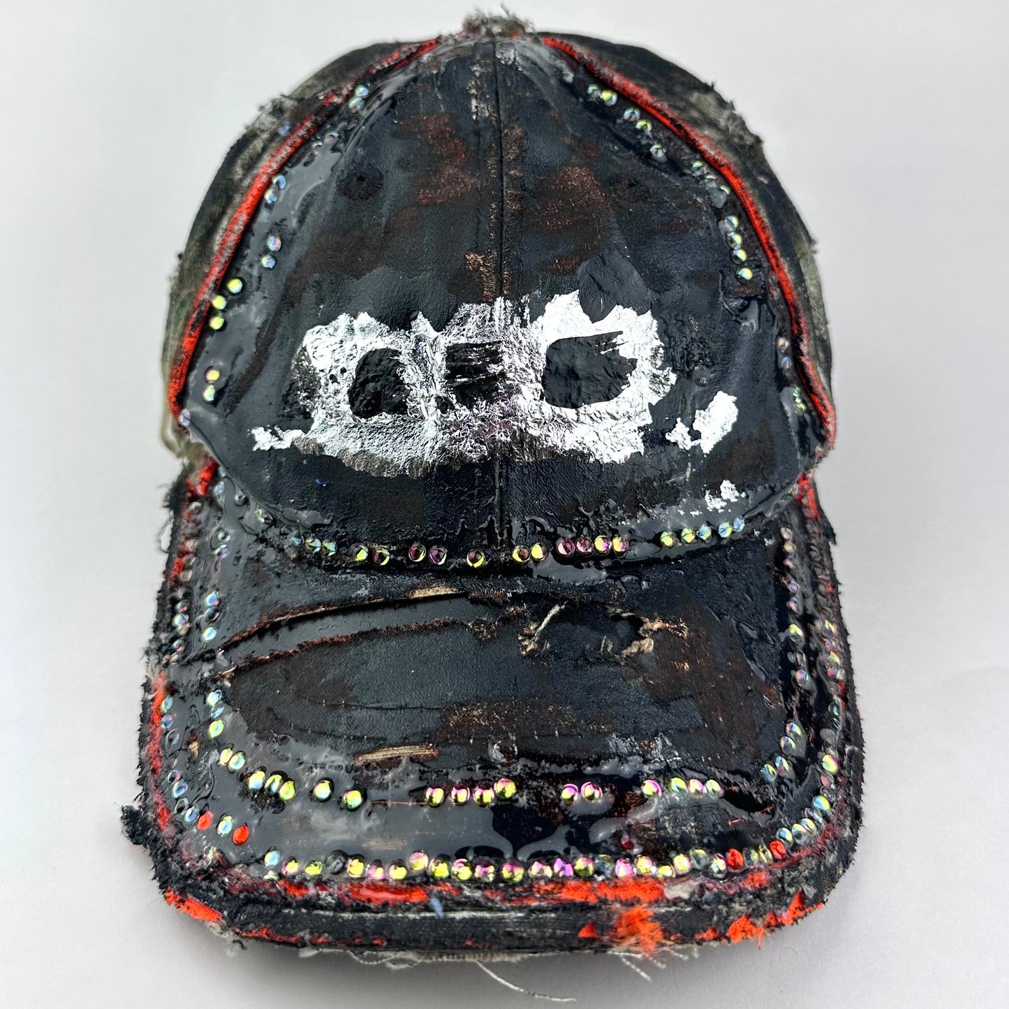 Front of ASTROBOI* brown camouflage distressed hat with rhinestones sealed in clear resin and custom hand-painted detailing.