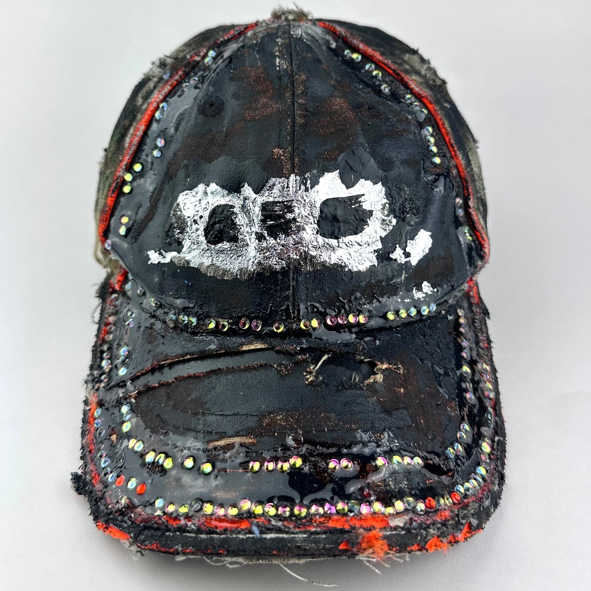 Front of ASTROBOI* brown camouflage distressed hat with rhinestones sealed in clear resin and custom hand-painted detailing.