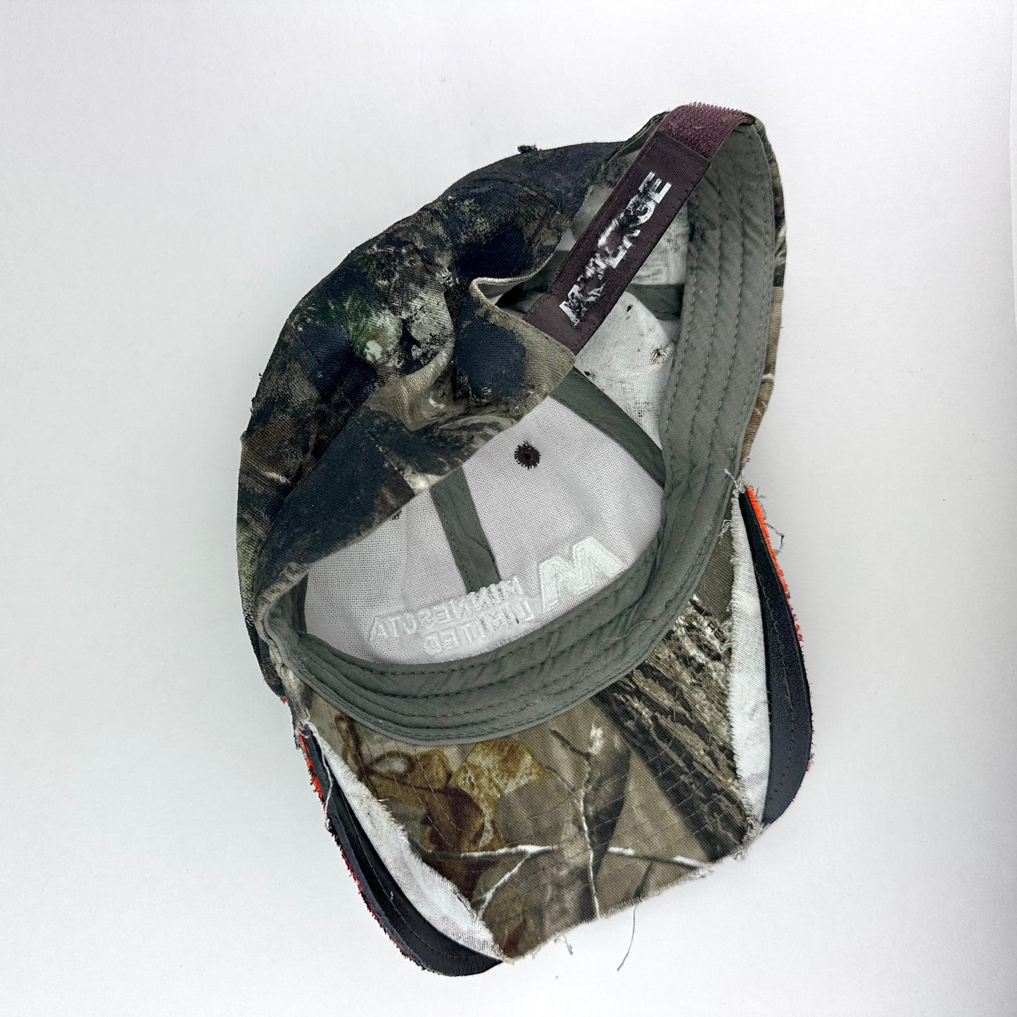 Flay lay back side on of ASTROBOI* brown camouflage distressed hat with rhinestones sealed in clear resin and custom hand-painted detailing.