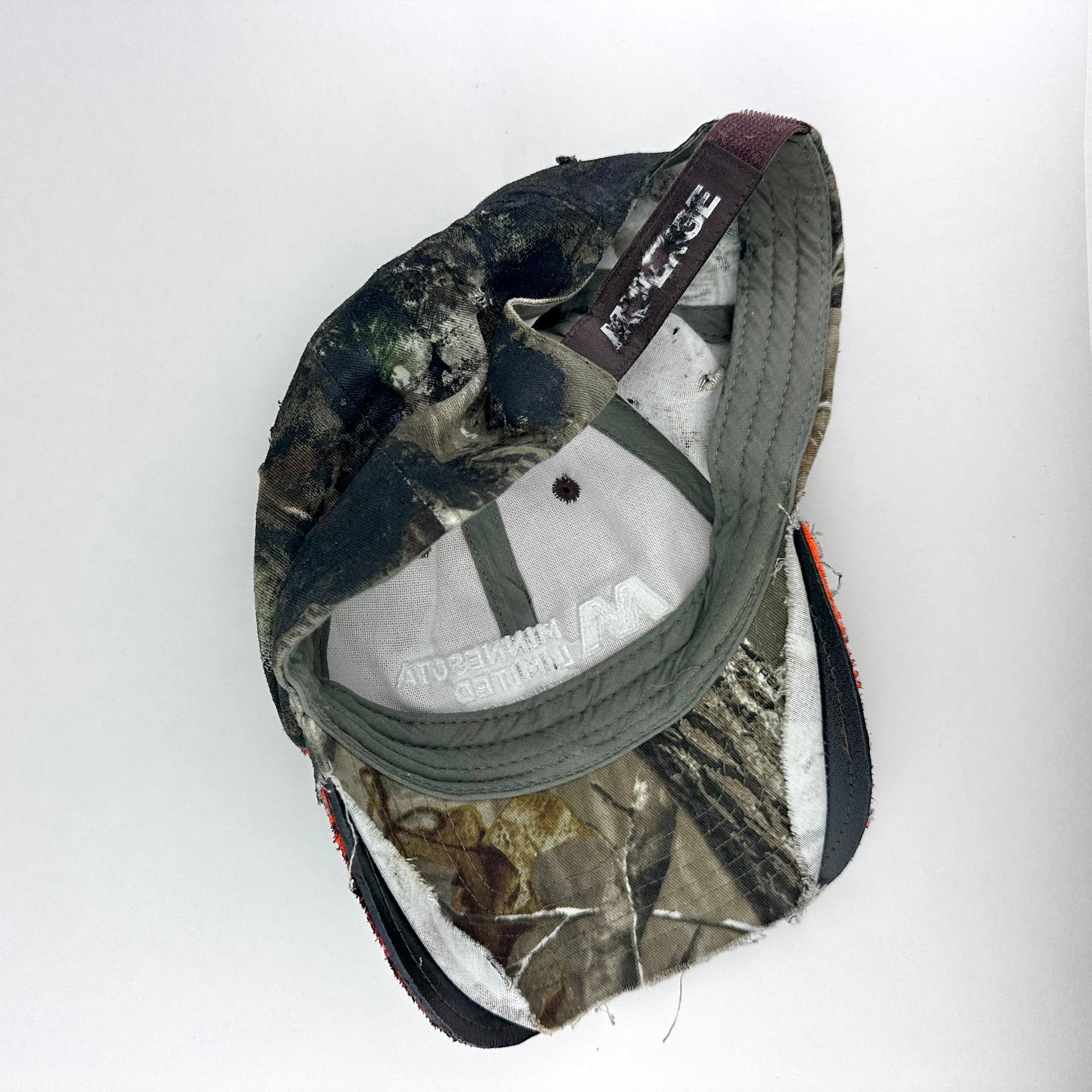 Flay lay back side on of ASTROBOI* brown camouflage distressed hat with rhinestones sealed in clear resin and custom hand-painted detailing.