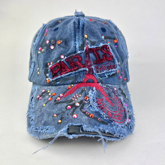 Front of ASTROBOI* Lights of Paris blue baseball hat with Eiffel Tower embroidery, black graffiti print and red orange rhinestone crystals.