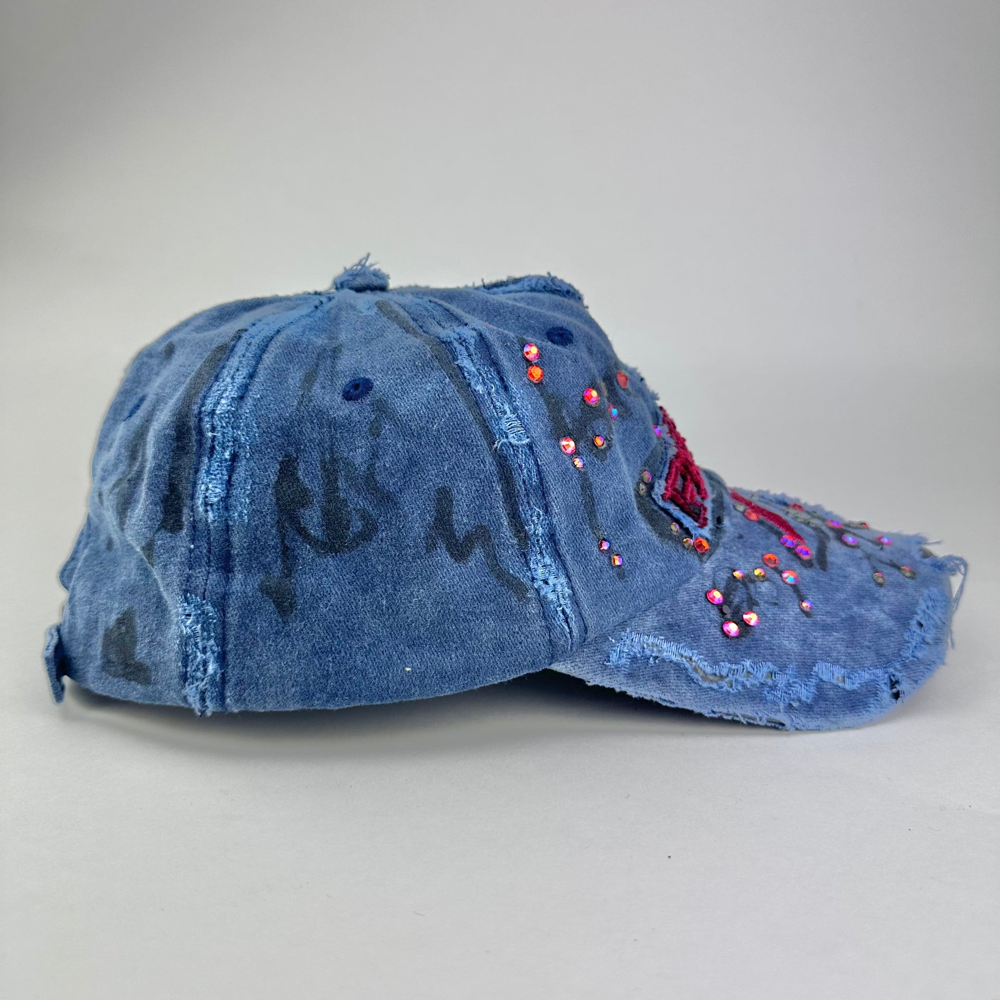 Right side of ASTROBOI* Lights of Paris blue baseball hat with Eiffel Tower embroidery, black graffiti print and red orange rhinestone crystals.