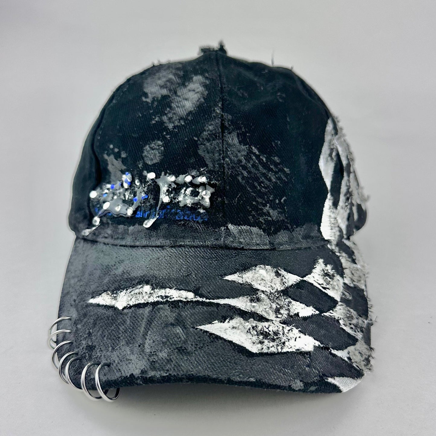 Flay lay overview of ASTROBOI* Speed Racing black and white checkered utility hat with resin-set rhinestones, stainless steel piercings, and hand-painted detailing