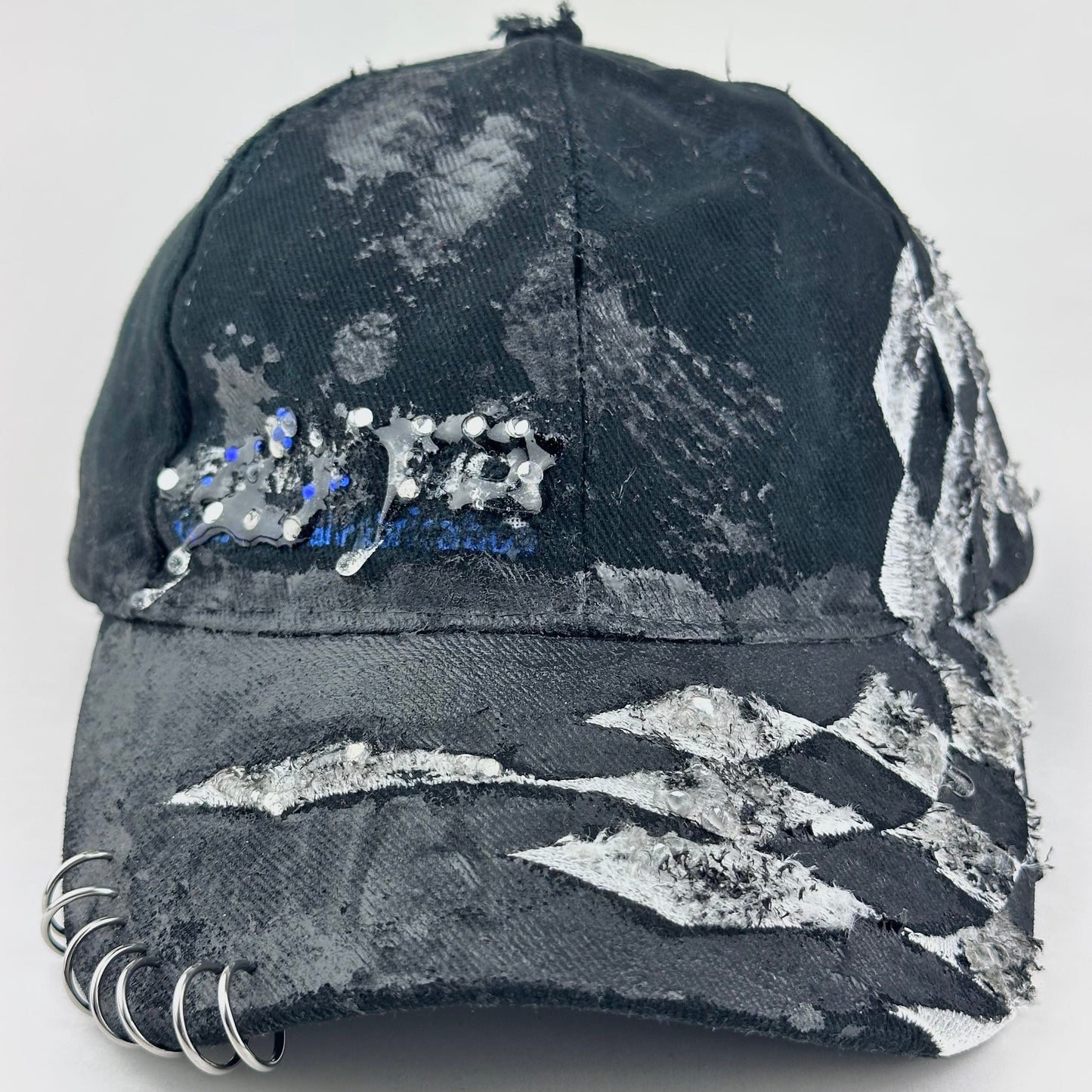 Front flay lay of of ASTROBOI* Speed Racing black and white checkered utility hat with resin-set rhinestones, stainless steel piercings, and hand-painted detailing