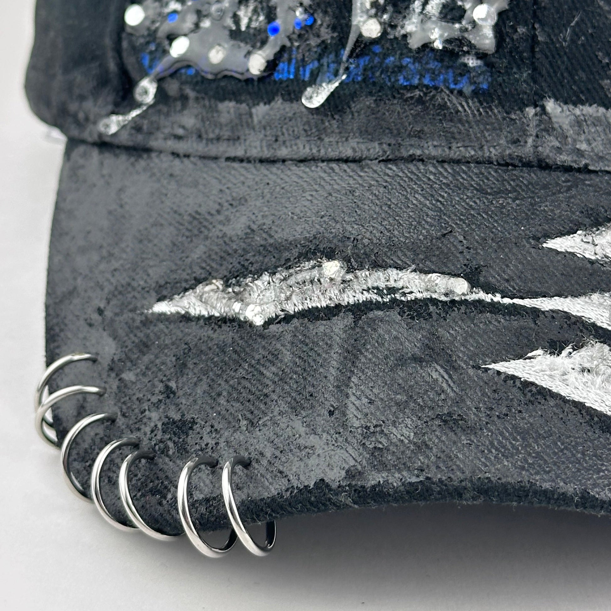 Flay lay piercing details on ASTROBOI* Speed Racing black and white checkered utility hat with resin-set rhinestones, stainless steel piercings, and hand-painted detailing