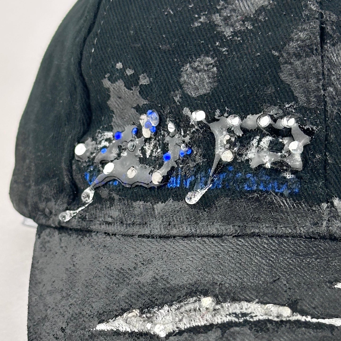 Flay lay logo detail of ASTROBOI* Speed Racing black and white checkered utility hat with resin-set rhinestones, stainless steel piercings, and hand-painted detailing