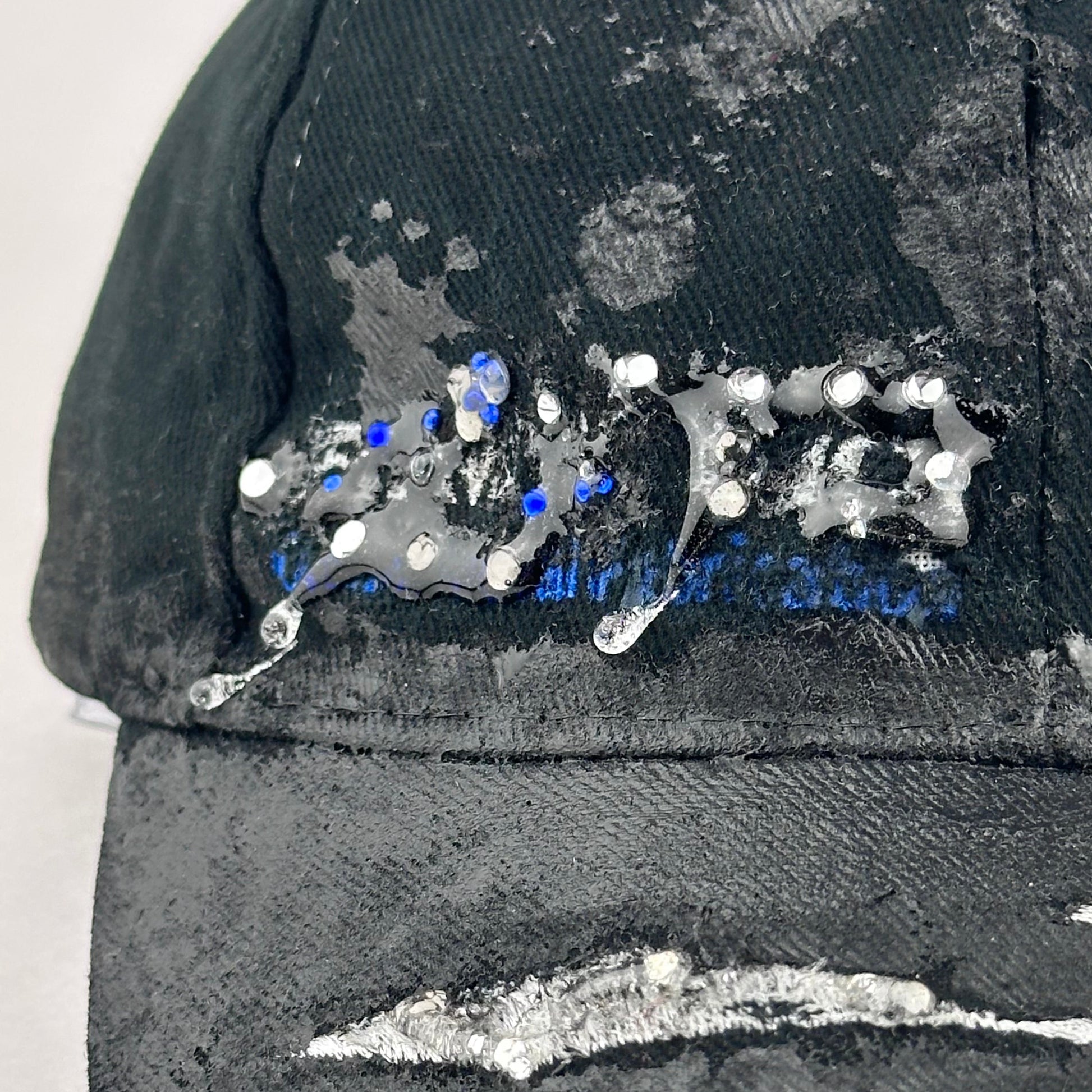 Flay lay logo detail of ASTROBOI* Speed Racing black and white checkered utility hat with resin-set rhinestones, stainless steel piercings, and hand-painted detailing