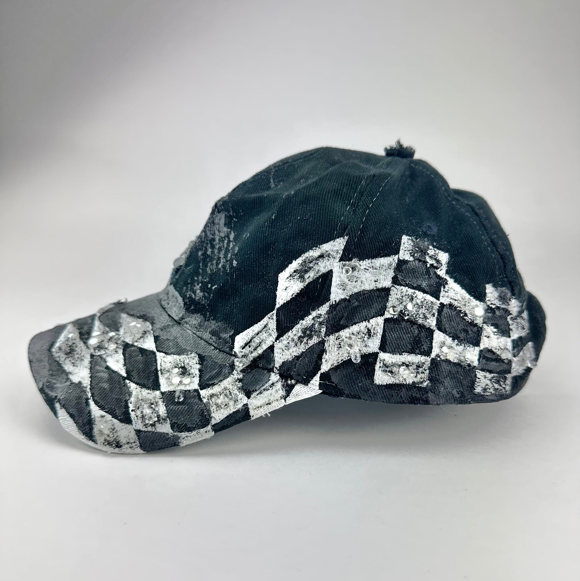Flay lay right side of ASTROBOI* Speed Racing black and white checkered utility hat with resin-set rhinestones, stainless steel piercings, and hand-painted detailing