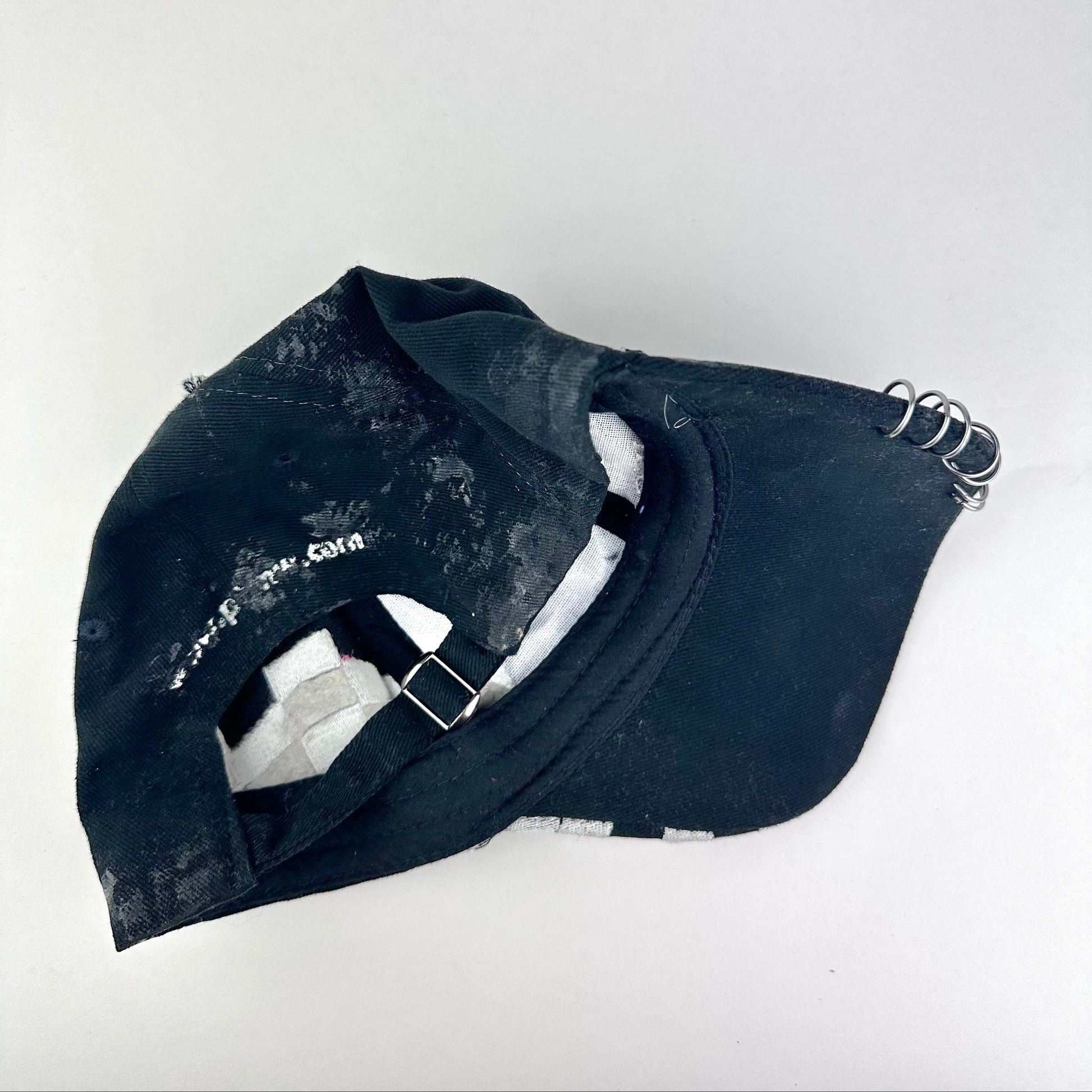 Flay lay back detail on ASTROBOI* Speed Racing black and white checkered utility hat with resin-set rhinestones, stainless steel piercings, and hand-painted detailing