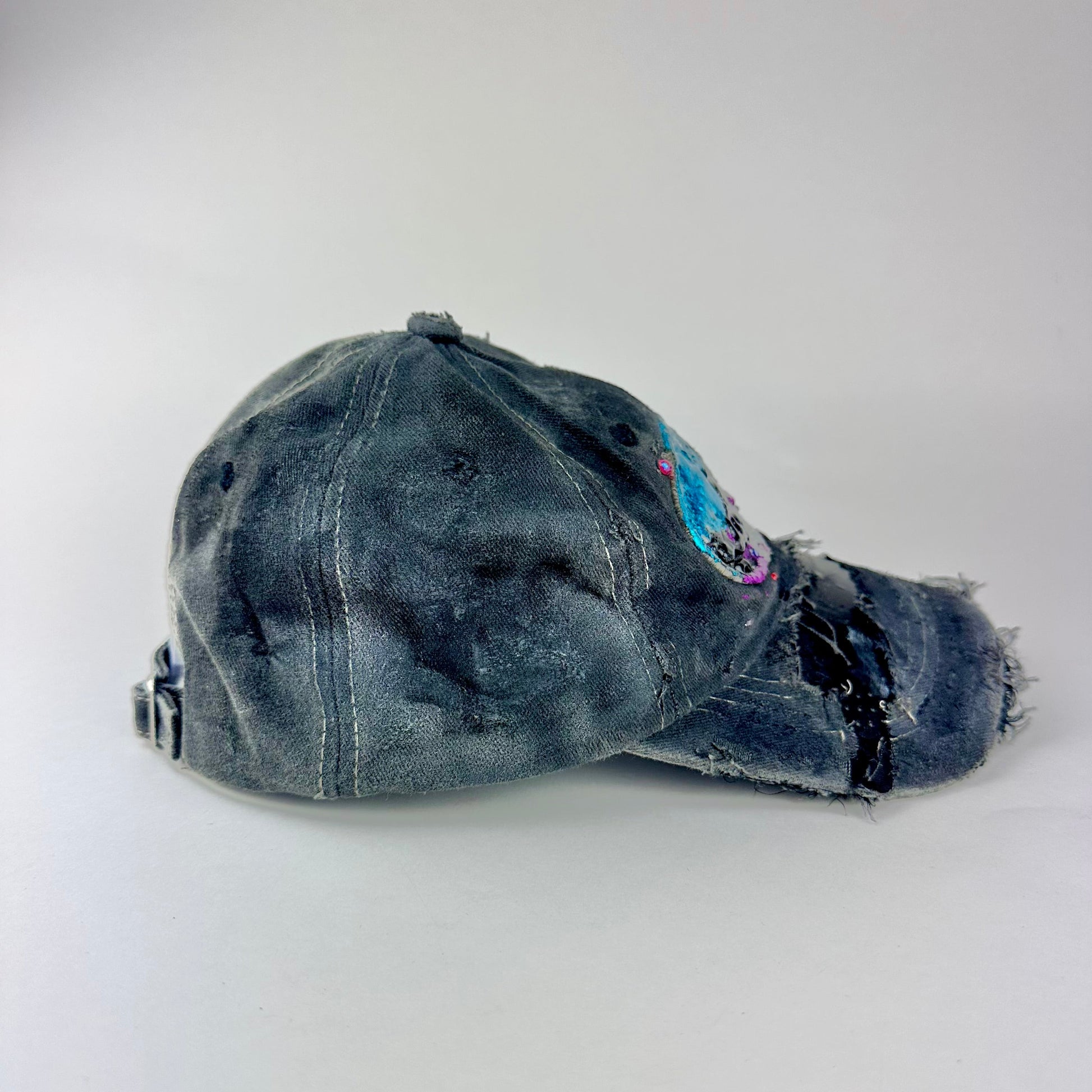 Right side of ASTROBOI* Technicolor black distressed hat with multicolor metallic New Orleans logo, rhinestones sealed in resin and ripped visor detail.