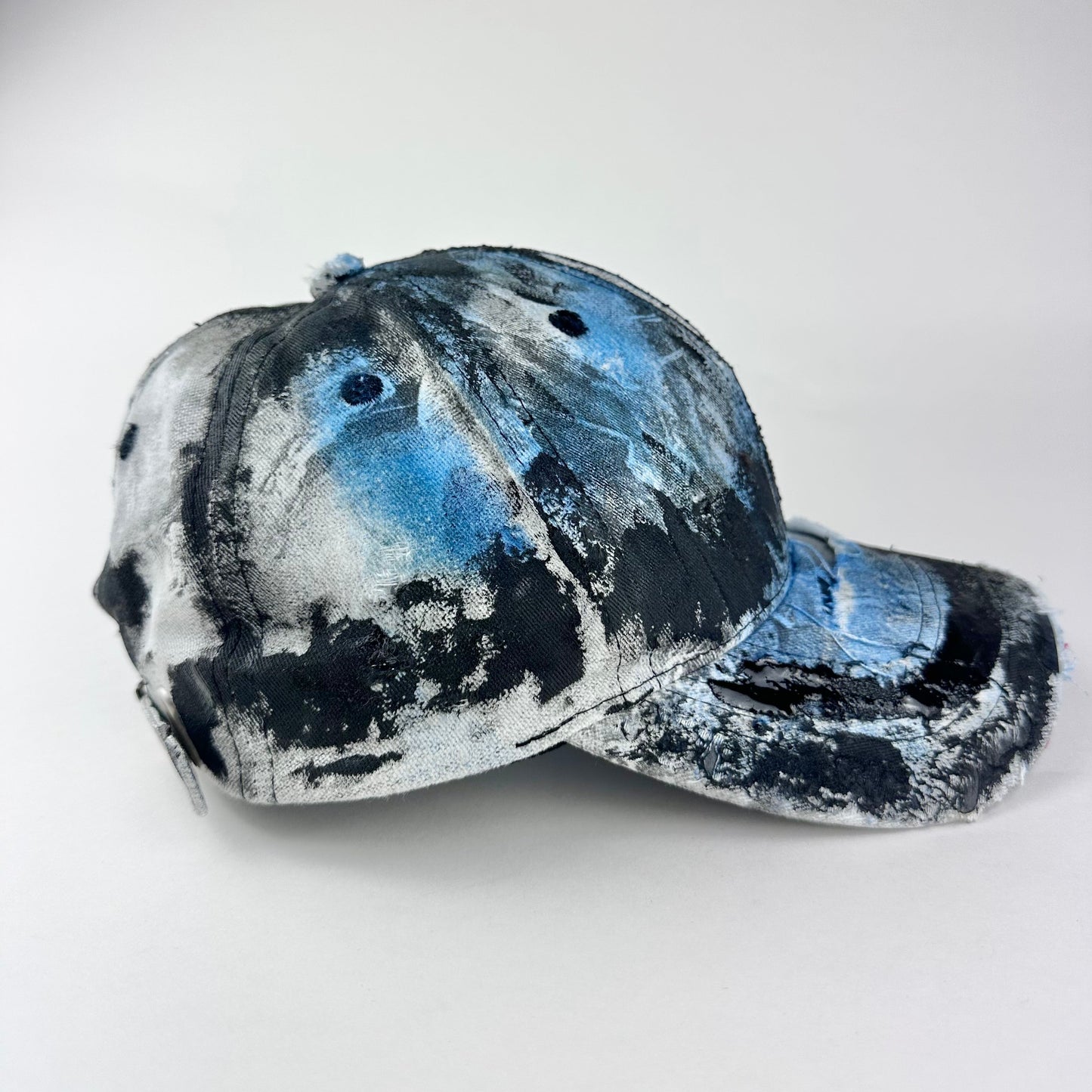 Right side of ASTROBOI* white trompe l’oeil denim print hat with blue and black paint, resin accents, and distressed detailing.
