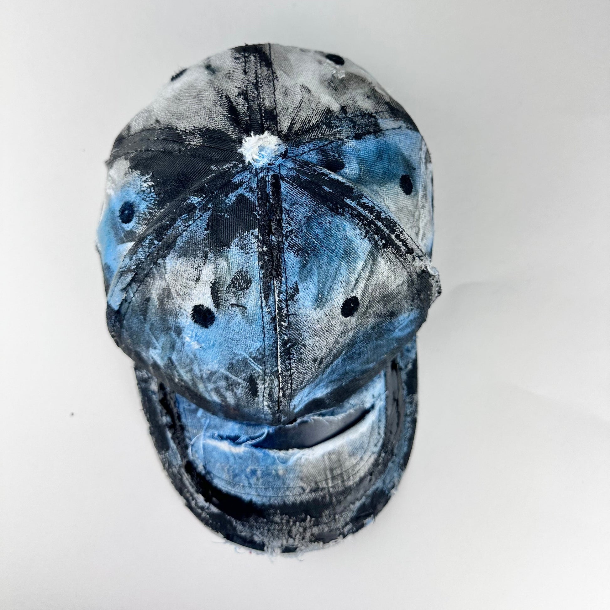 Top of ASTROBOI* white trompe l’oeil denim print hat with blue and black paint, resin accents, and distressed detailing.