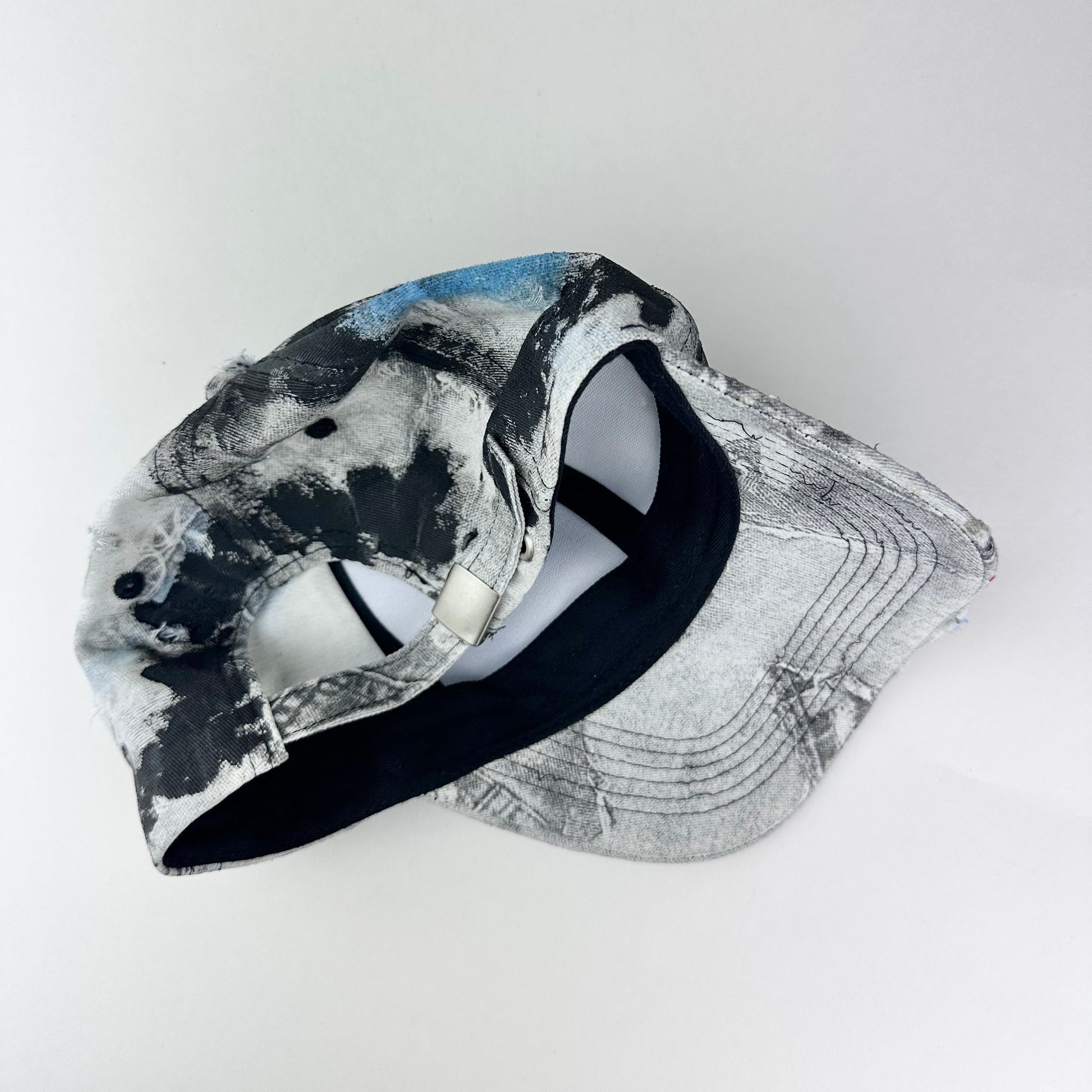 Back of ASTROBOI* white trompe l’oeil denim print hat with blue and black paint, resin accents, and distressed detailing.
