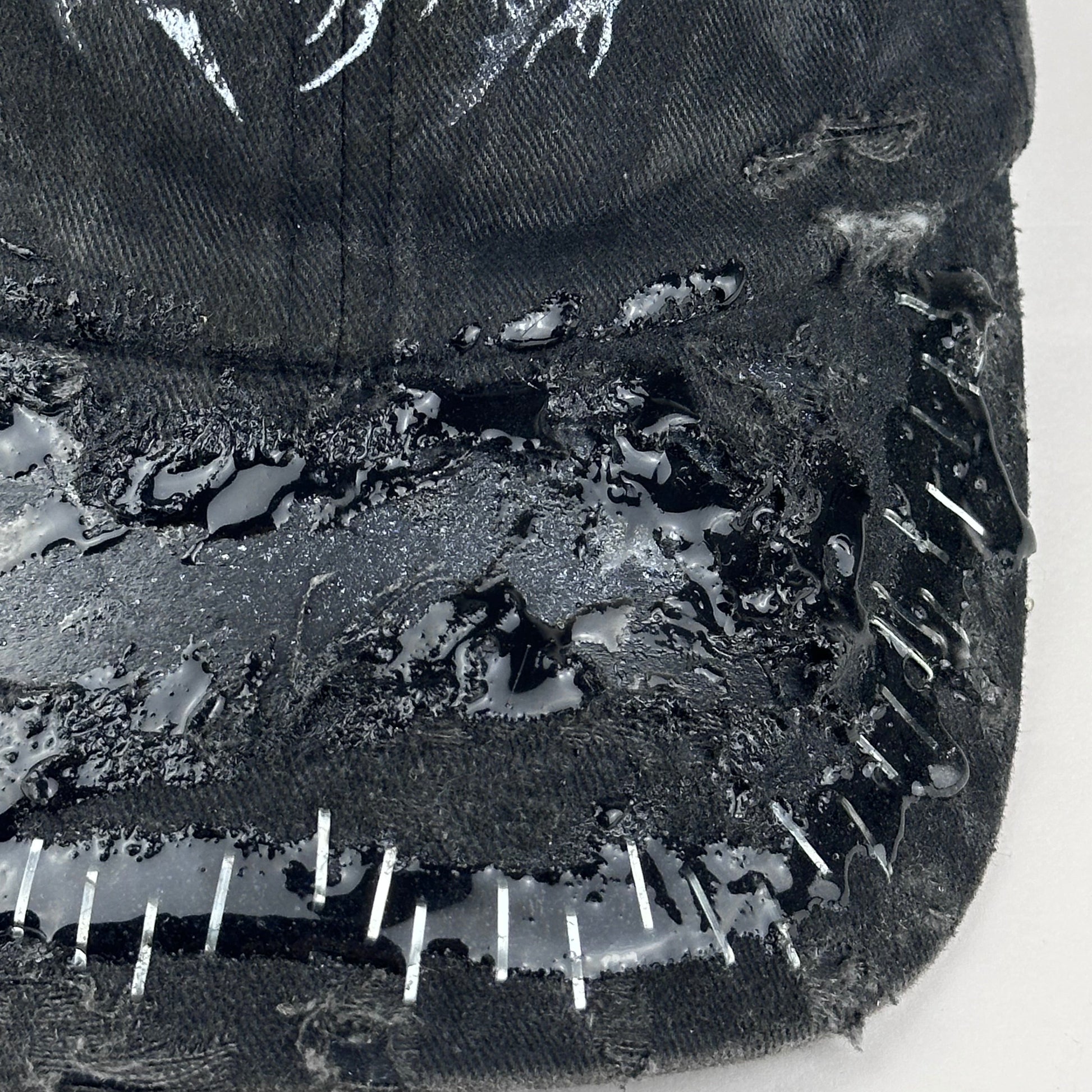 Details on ASTROBOI* Stitched Up black distressed hat with silver staples sealed in resin, indie logo, and custom paint, handmade in NYC.