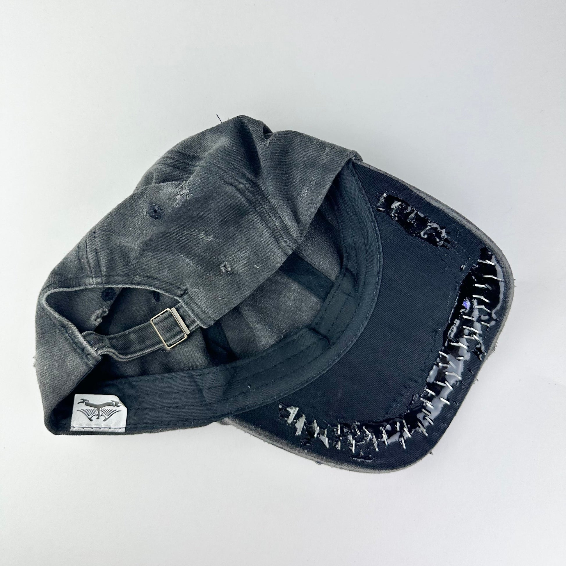 Back of ASTROBOI* Stitched Up black distressed hat with silver staples sealed in resin, indie logo, and custom paint, handmade in NYC.