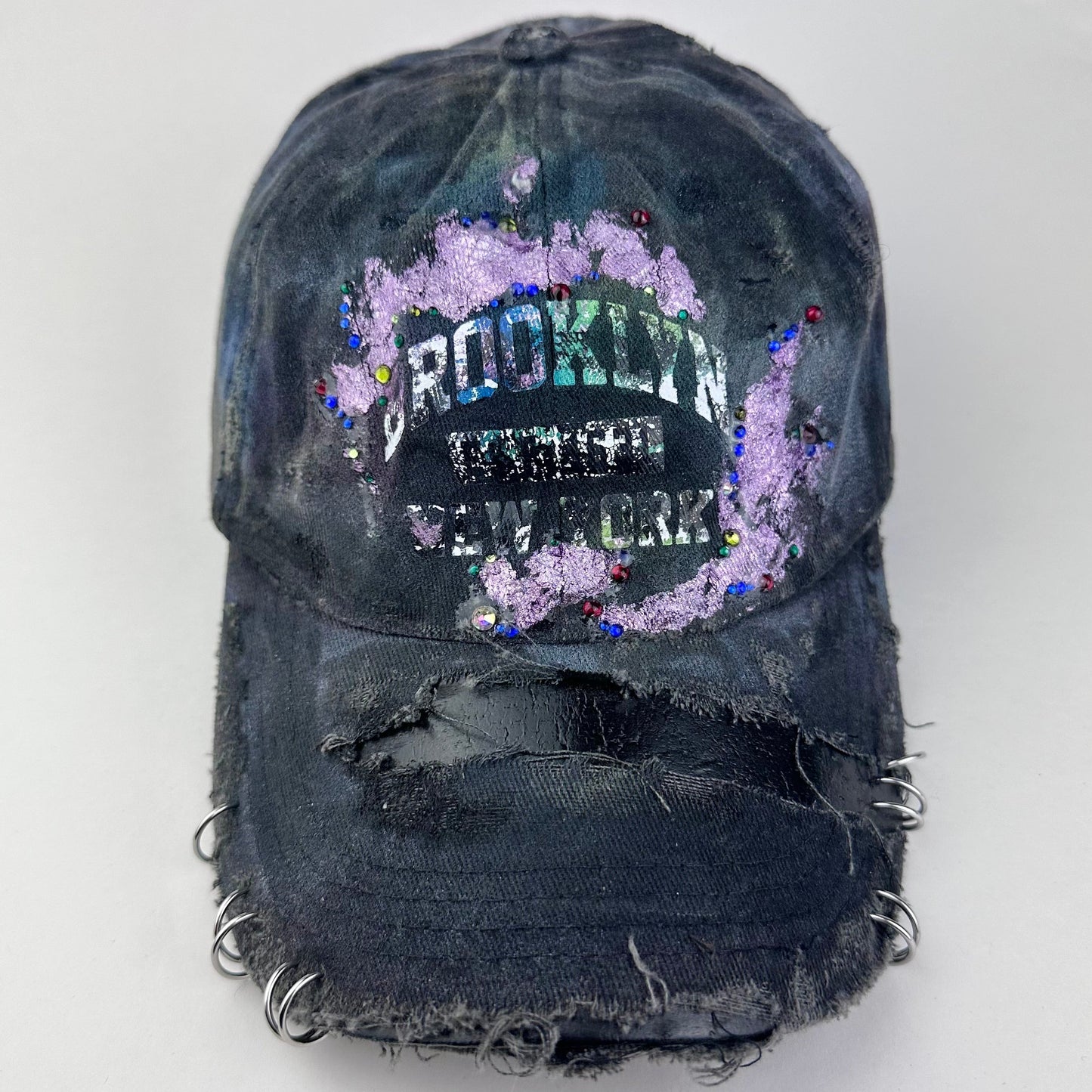 Cover image of ASTROBOI* distressed black Brooklyn hat with metallic purple paint, multicolored rhinestones, green airbrush shading, and white front lettering.