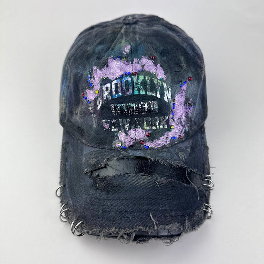 Cover image of ASTROBOI* distressed black Brooklyn hat with metallic purple paint, multicolored rhinestones, green airbrush shading, and white front lettering.