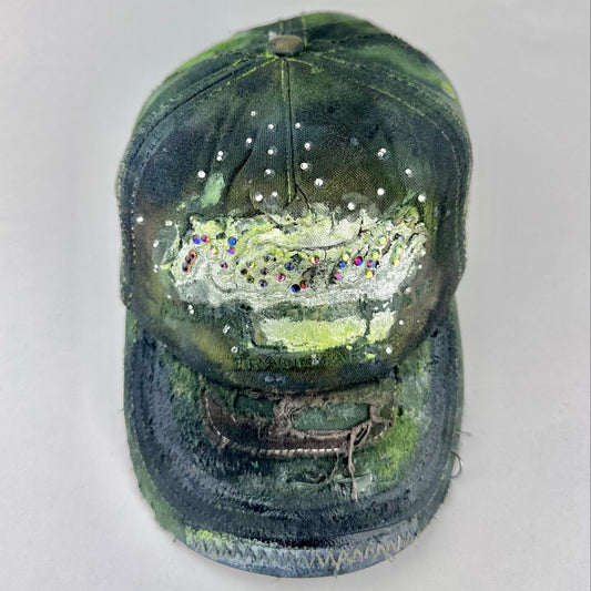 Front of “Green and brown distressed ASTROBOI* Hawaii hat with rhinestones, metallic paint, and sterling-steel piercings, customized in NYC.”