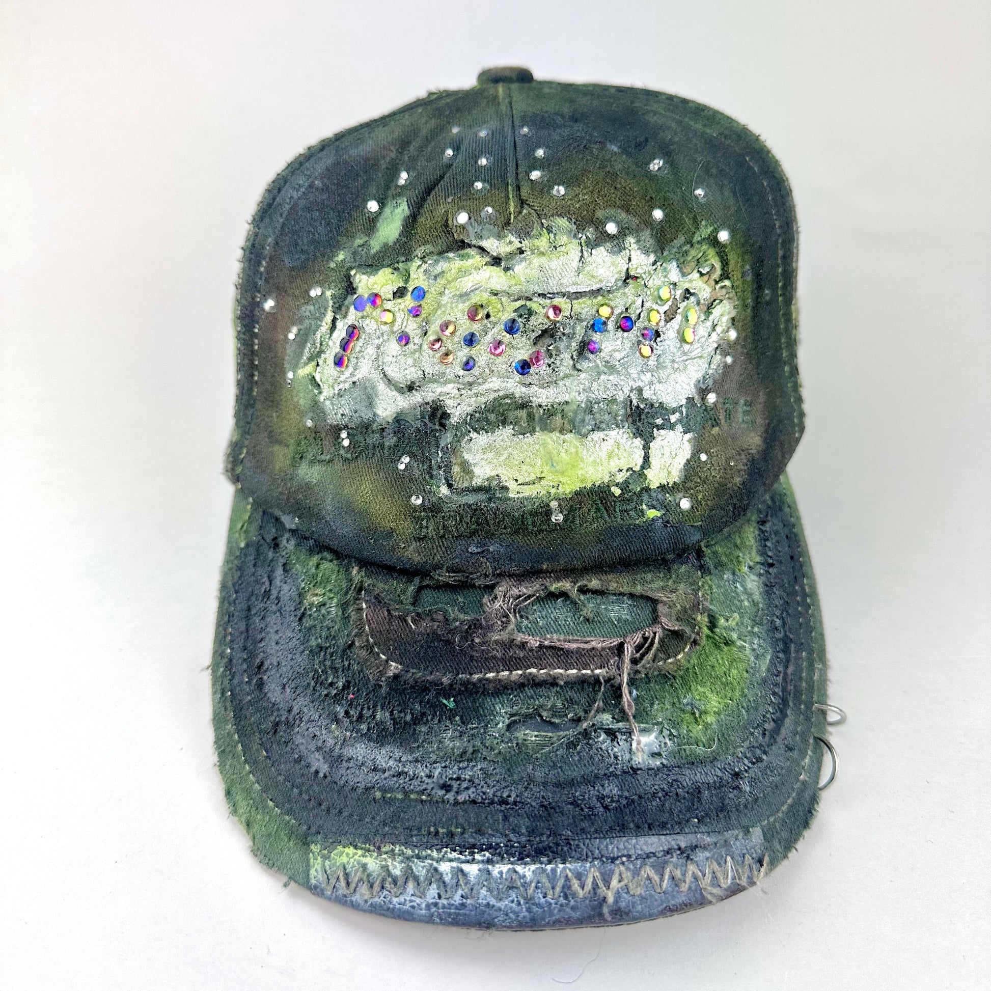 Front 2 of “Green and brown distressed ASTROBOI* Hawaii hat with rhinestones, metallic paint, and sterling-steel piercings, customized in NYC.”