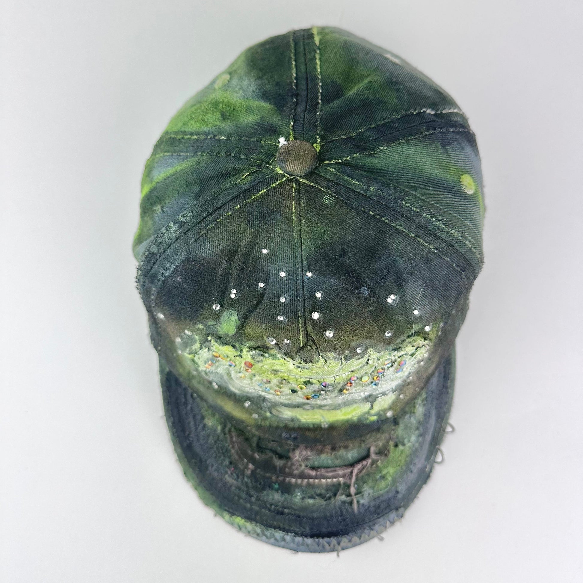 Top of “Green and brown distressed ASTROBOI* Hawaii hat with rhinestones, metallic paint, and sterling-steel piercings, customized in NYC.”