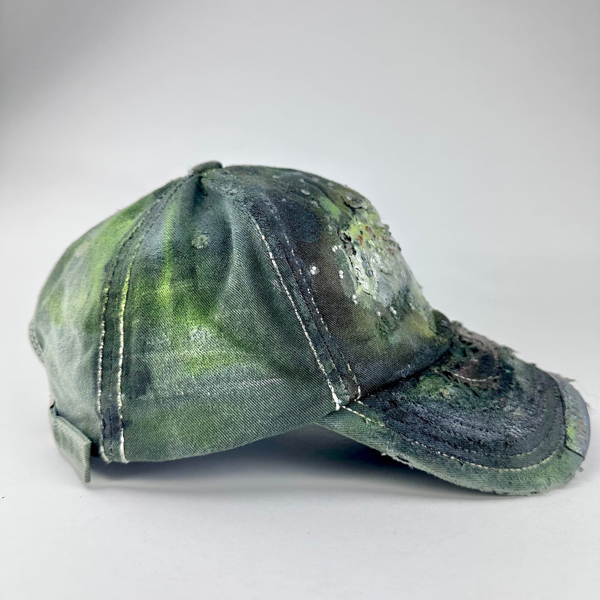 Right side of “Green and brown distressed ASTROBOI* Hawaii hat with rhinestones, metallic paint, and sterling-steel piercings, customized in NYC.”