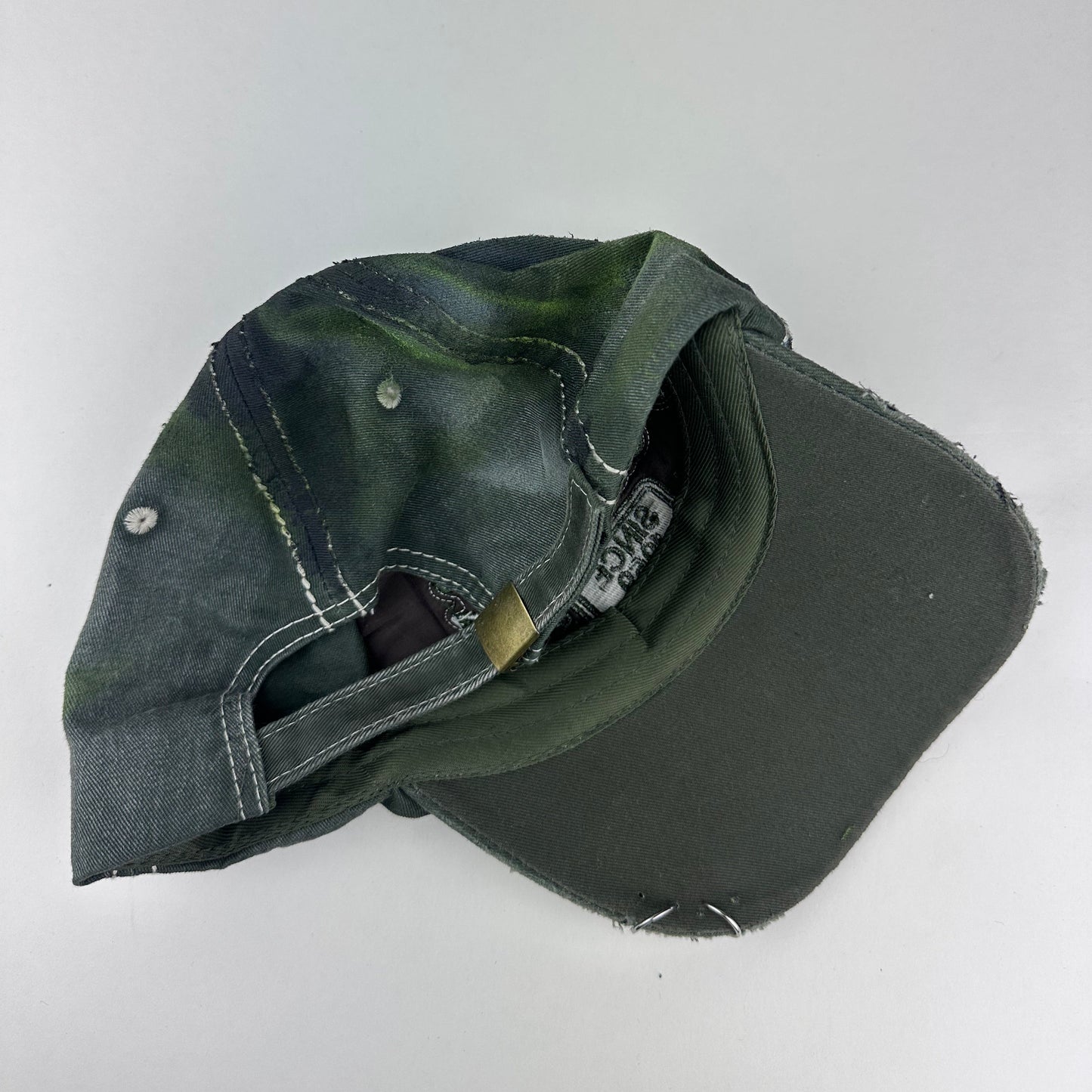 Back of “Green and brown distressed ASTROBOI* Hawaii hat with rhinestones, metallic paint, and sterling-steel piercings, customized in NYC.”