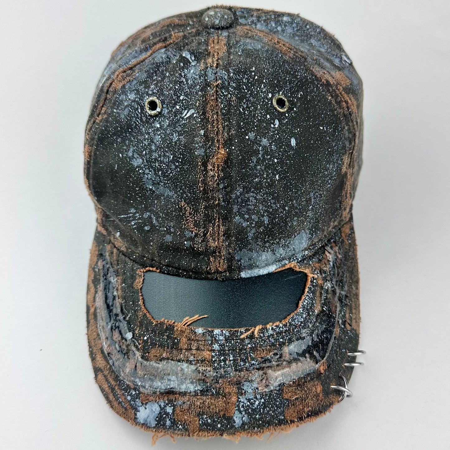 Cover image of ASTROBOI* brown distressed leather hat with white paint splatter, stainless steel piercings on visor and glossy clear resin finish.